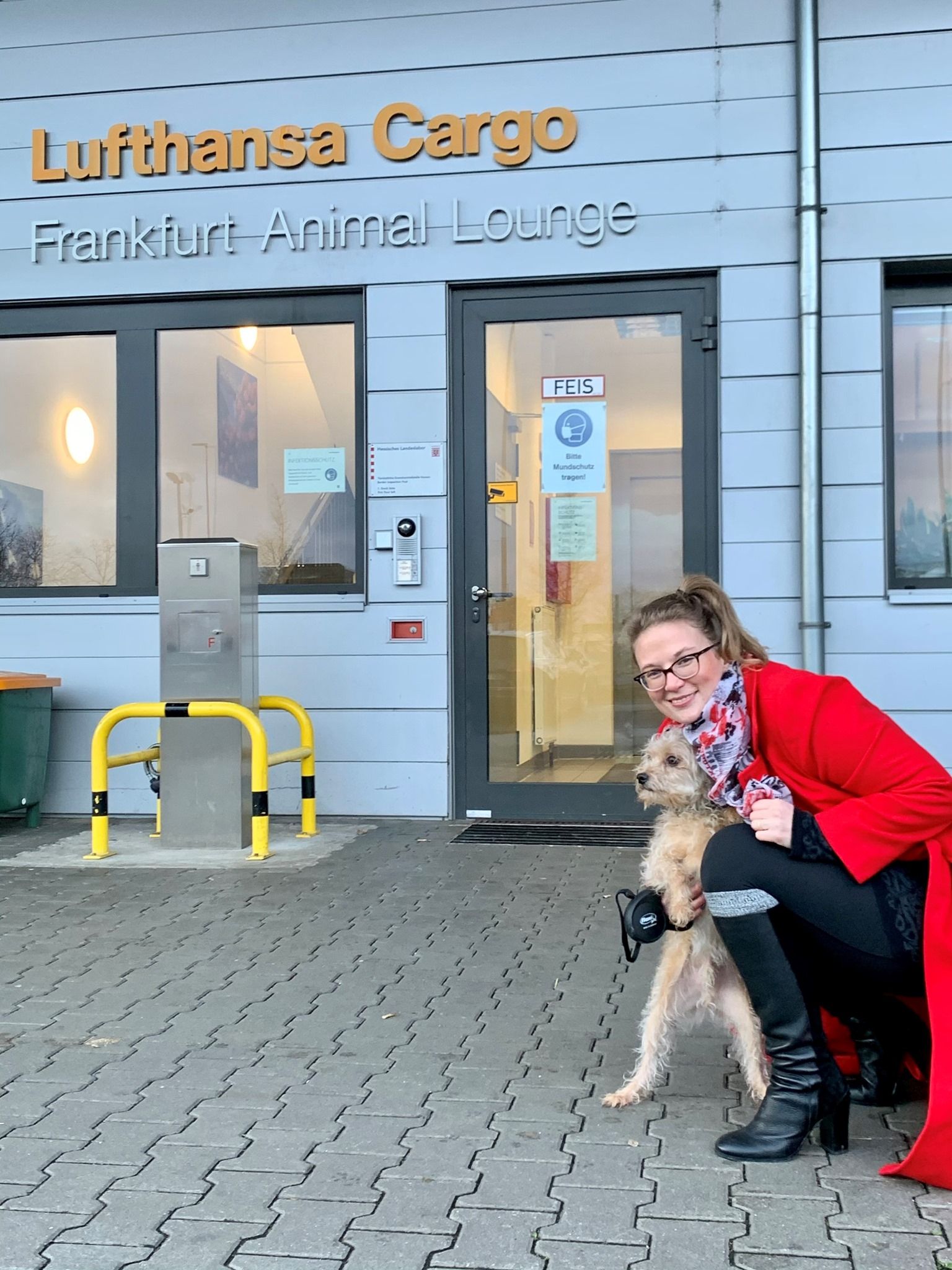 A woman is kneeling down with a dog in front of a building that says lufthansa cargo