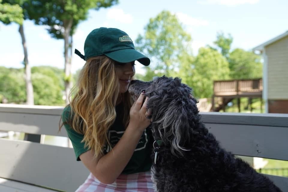A woman in a green hat is kissing a black dog