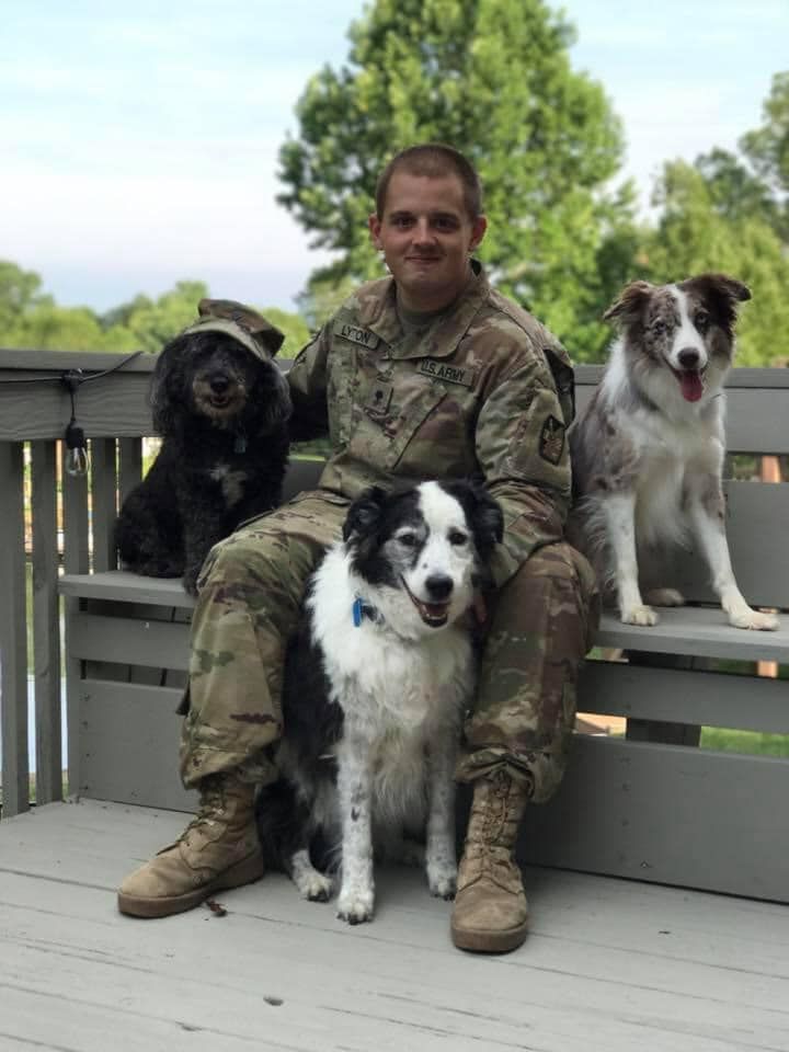 A man in a military uniform is sitting on a bench with three dogs.