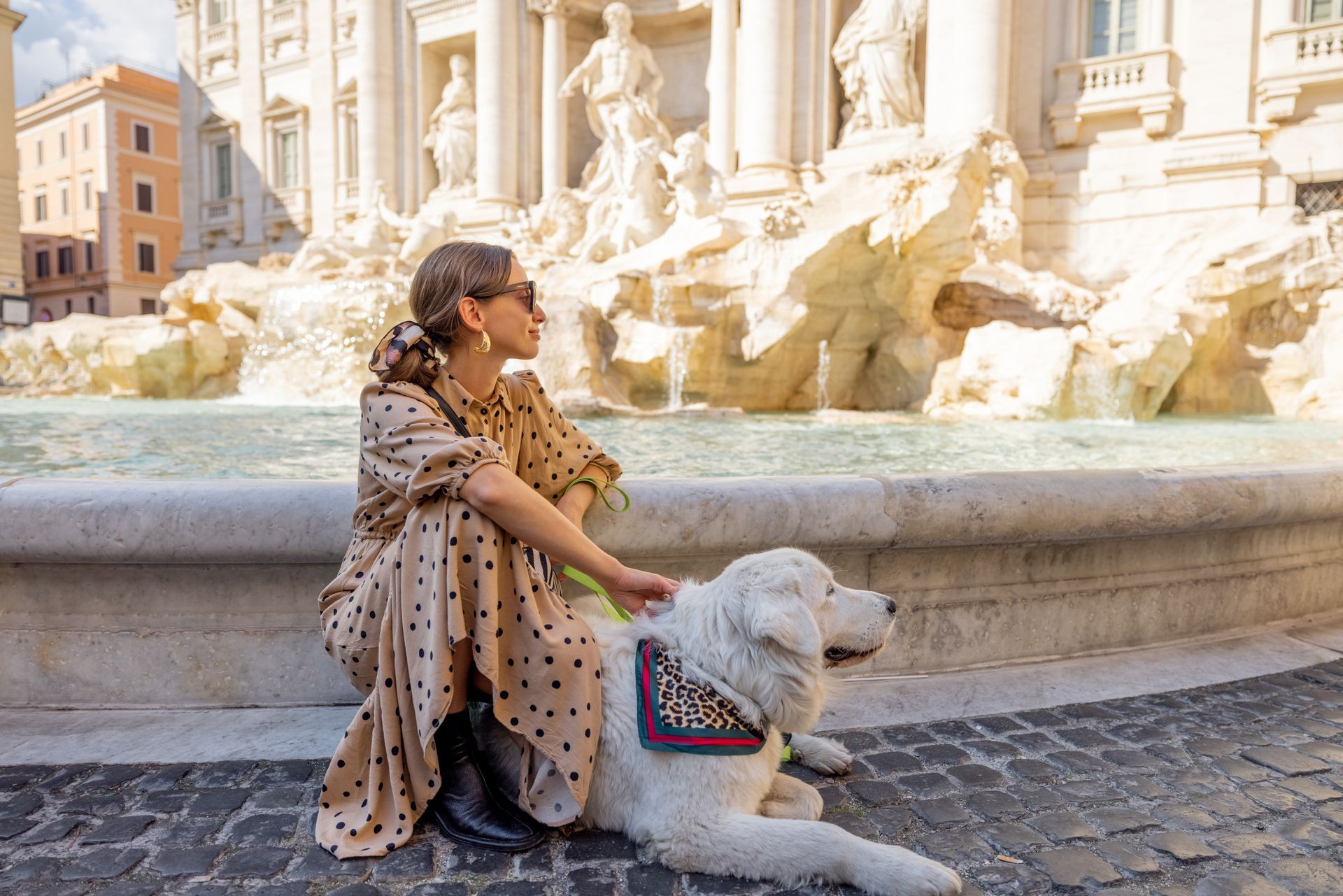A woman is sitting next to a dog in front of a fountain.