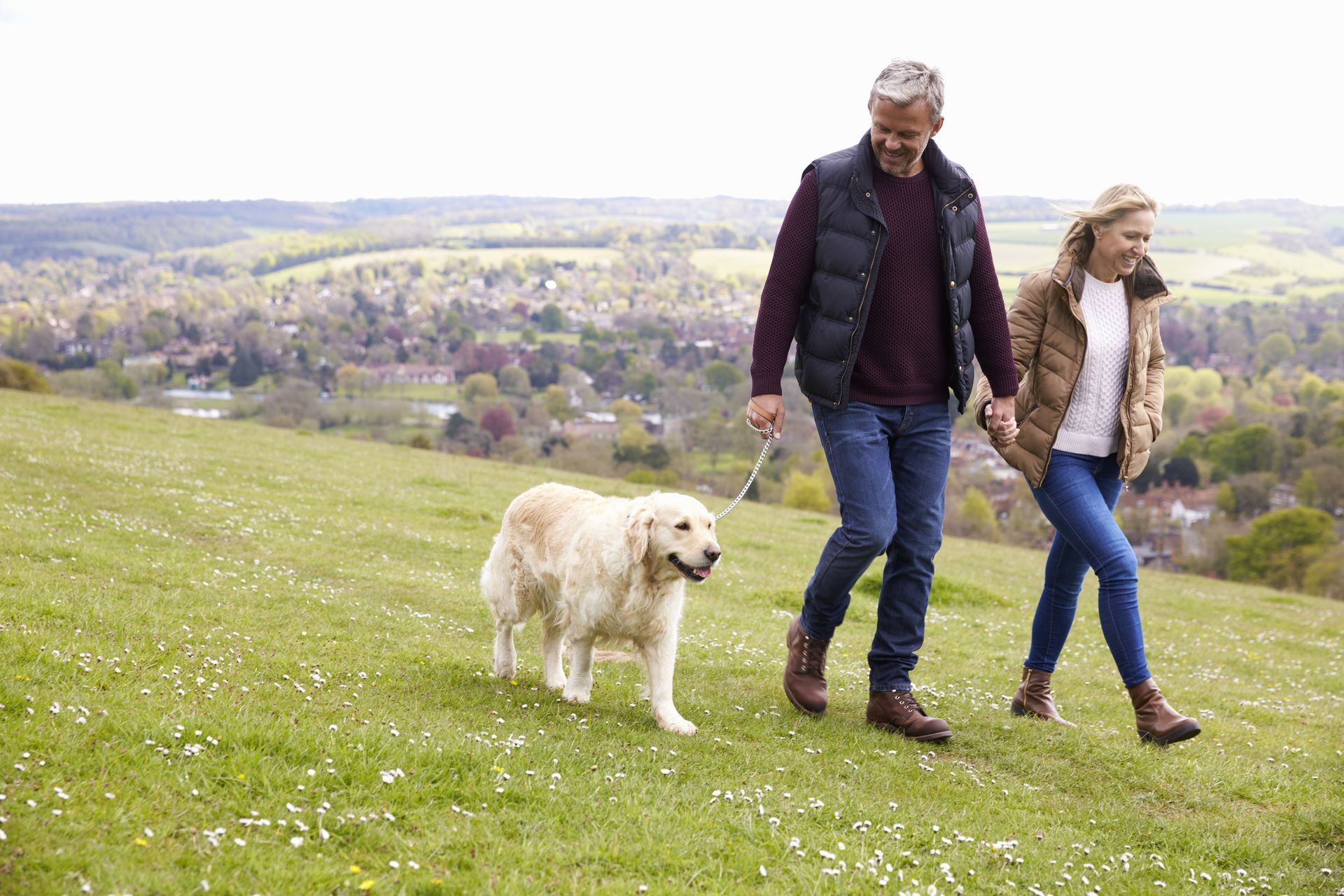 A man and woman are walking a dog on a leash in a field.