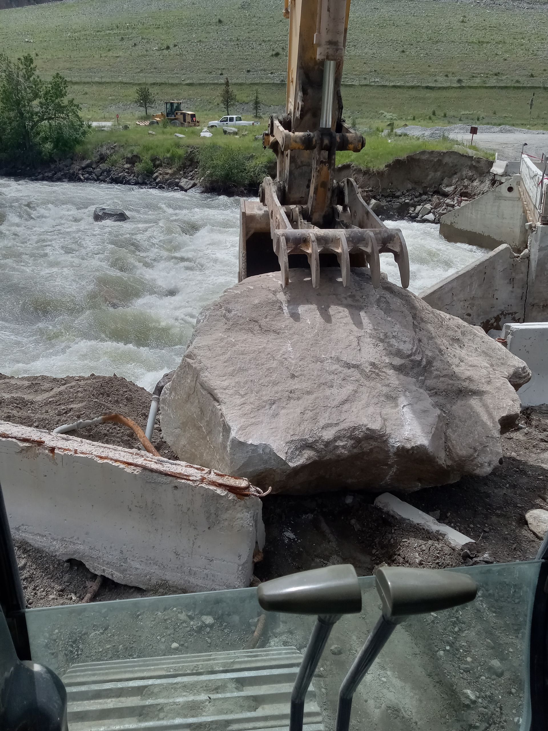 A large rock is being removed from a river by an excavator.