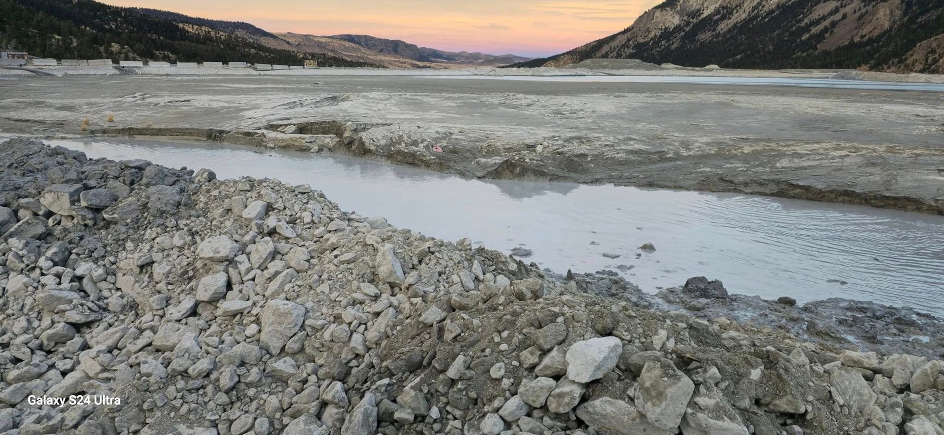 A large pile of rocks is sitting next to a river.