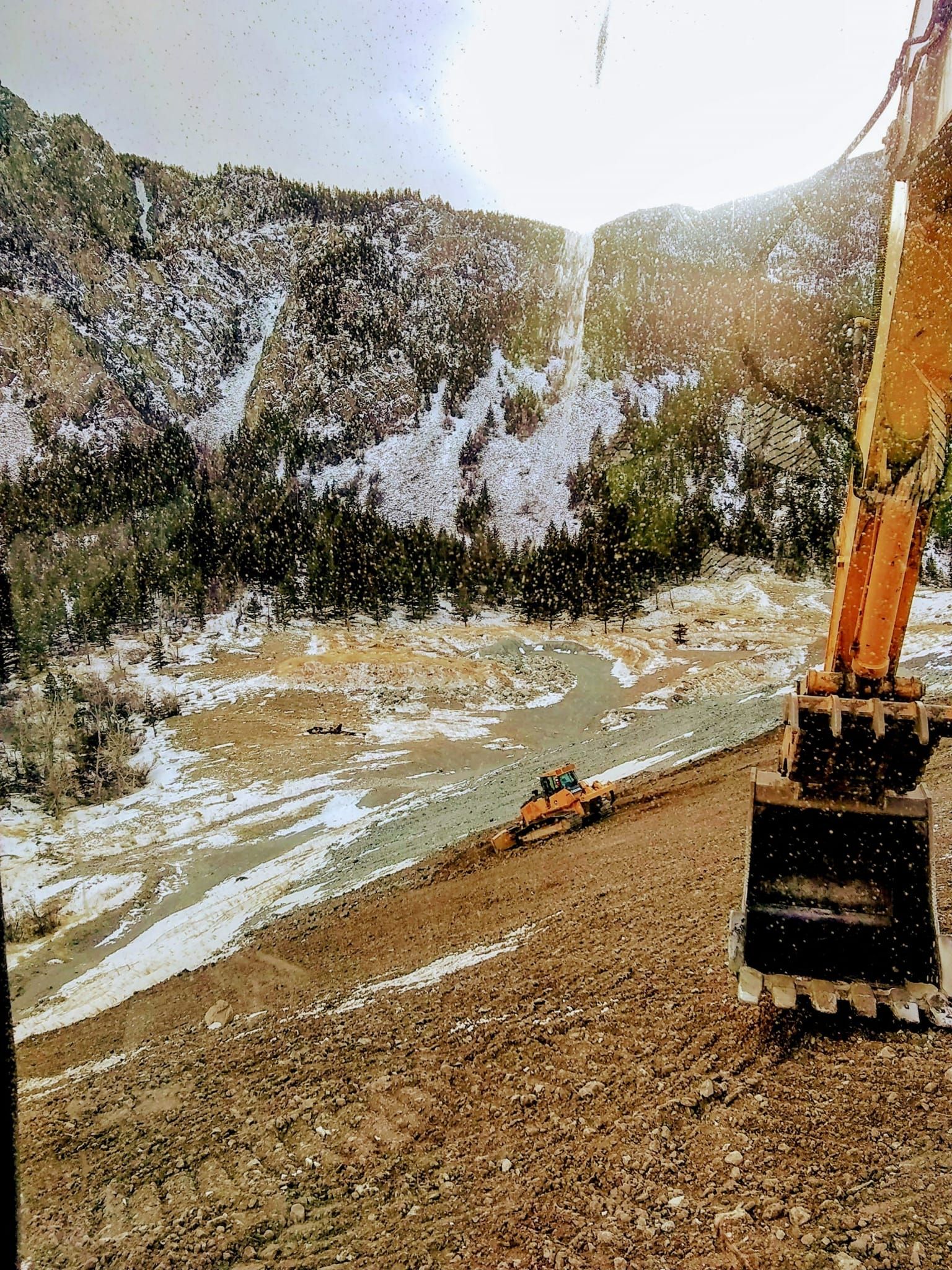 A large yellow excavator is sitting on top of a dirt field next to a river.