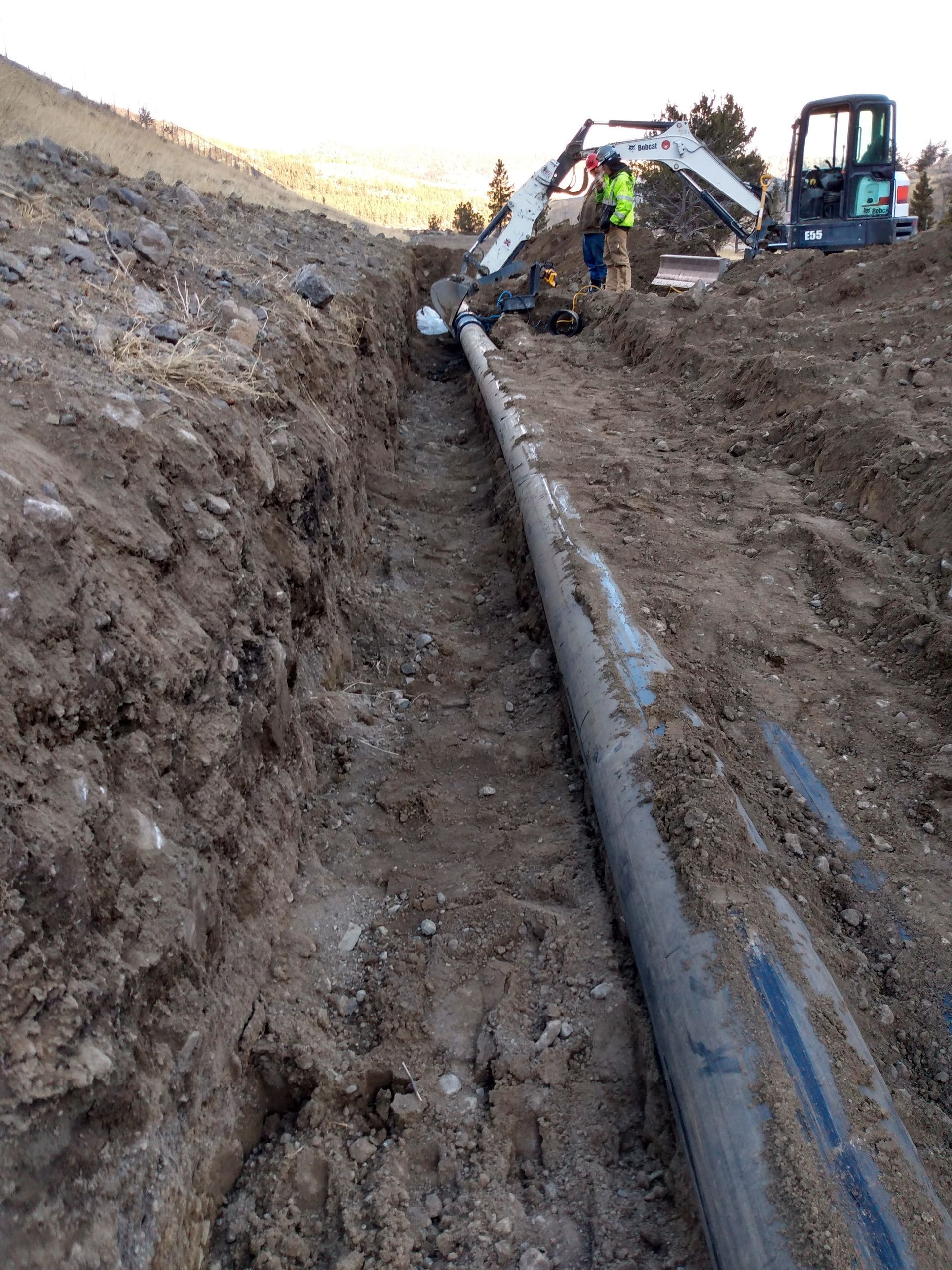 A man is standing next to a large pipe in the dirt.