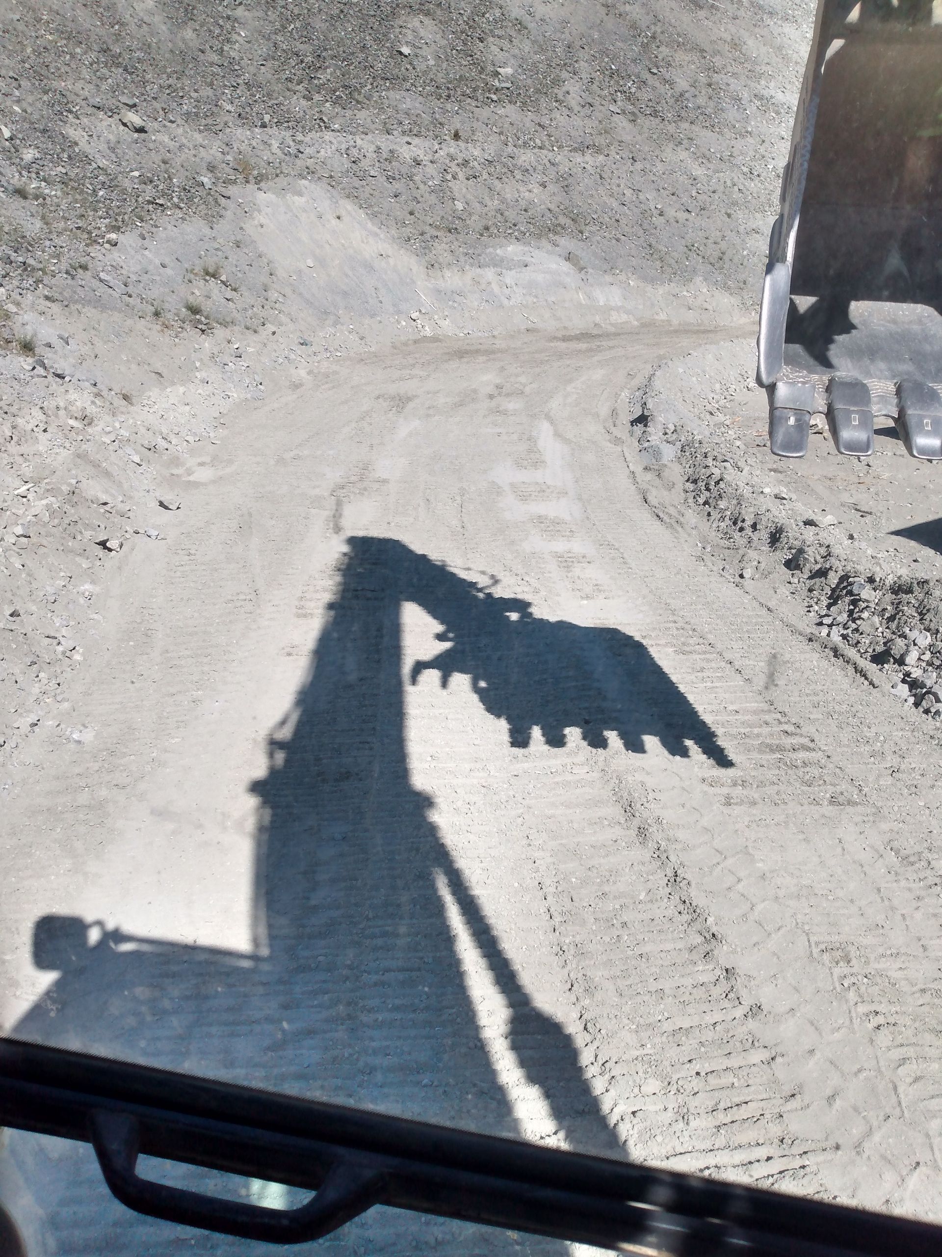 A shadow of a bulldozer is cast on a dirt road