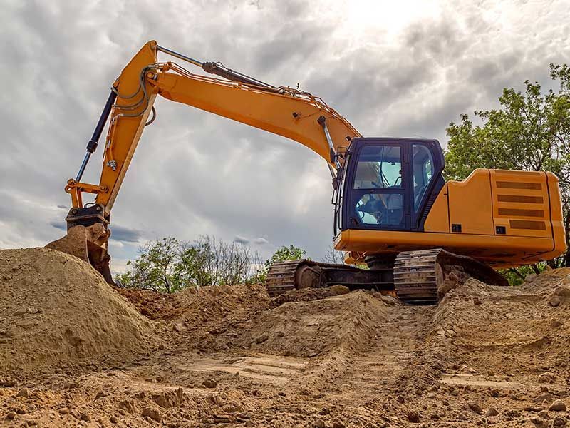 A yellow excavator is digging a hole in the dirt on a construction site.