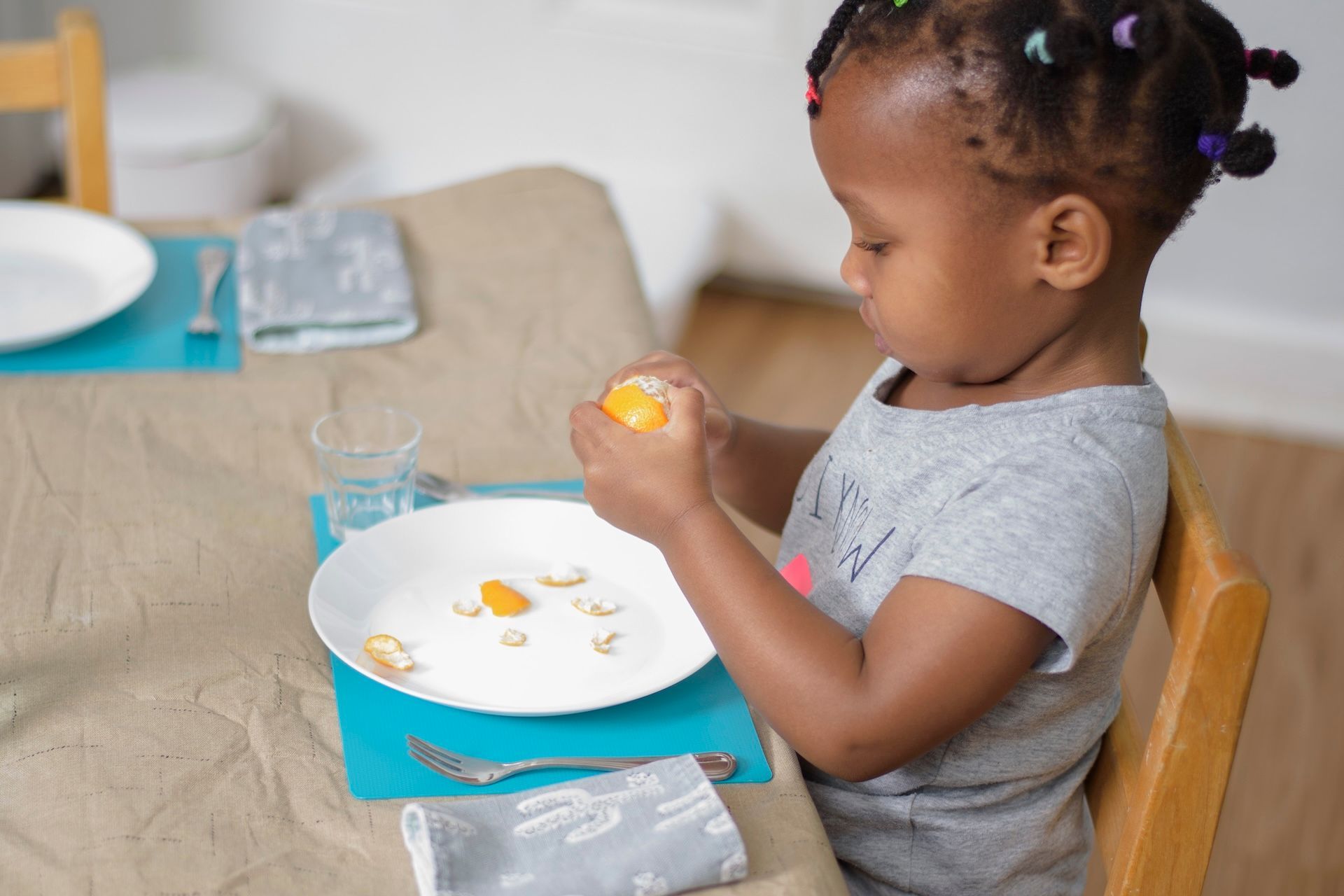 Child sitting at a table, holding a snack over a plate with a blue lunch box nearby.