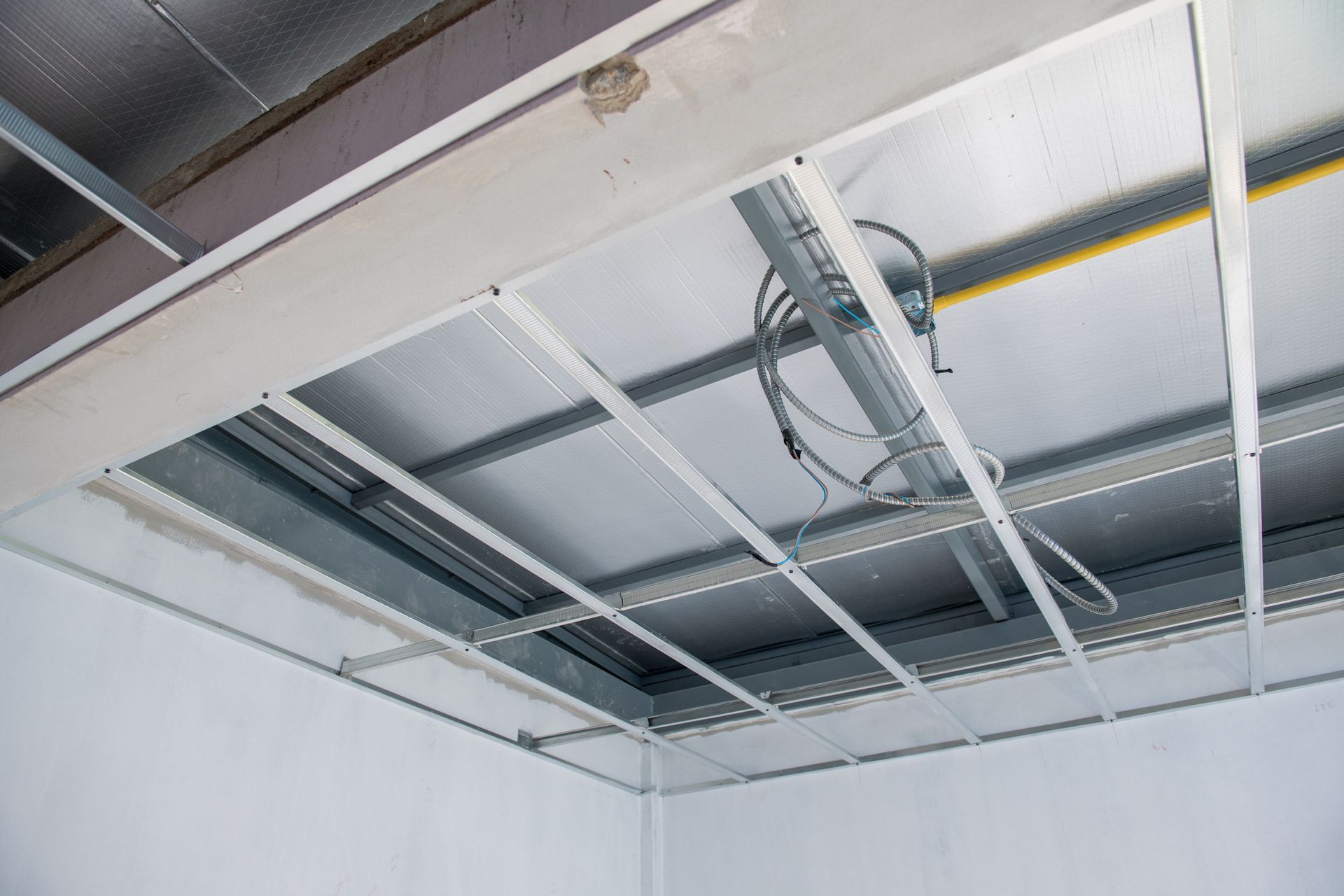 Metal grid ceiling under construction; wires and insulation visible above.