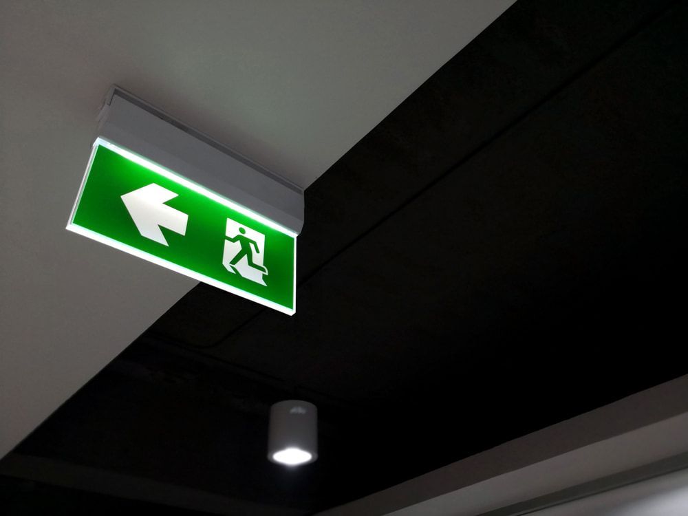 A Green Exit Sign Is Hanging from The Ceiling in A Dark Room — Brookes Engraving & Signs in Woonona, NSW