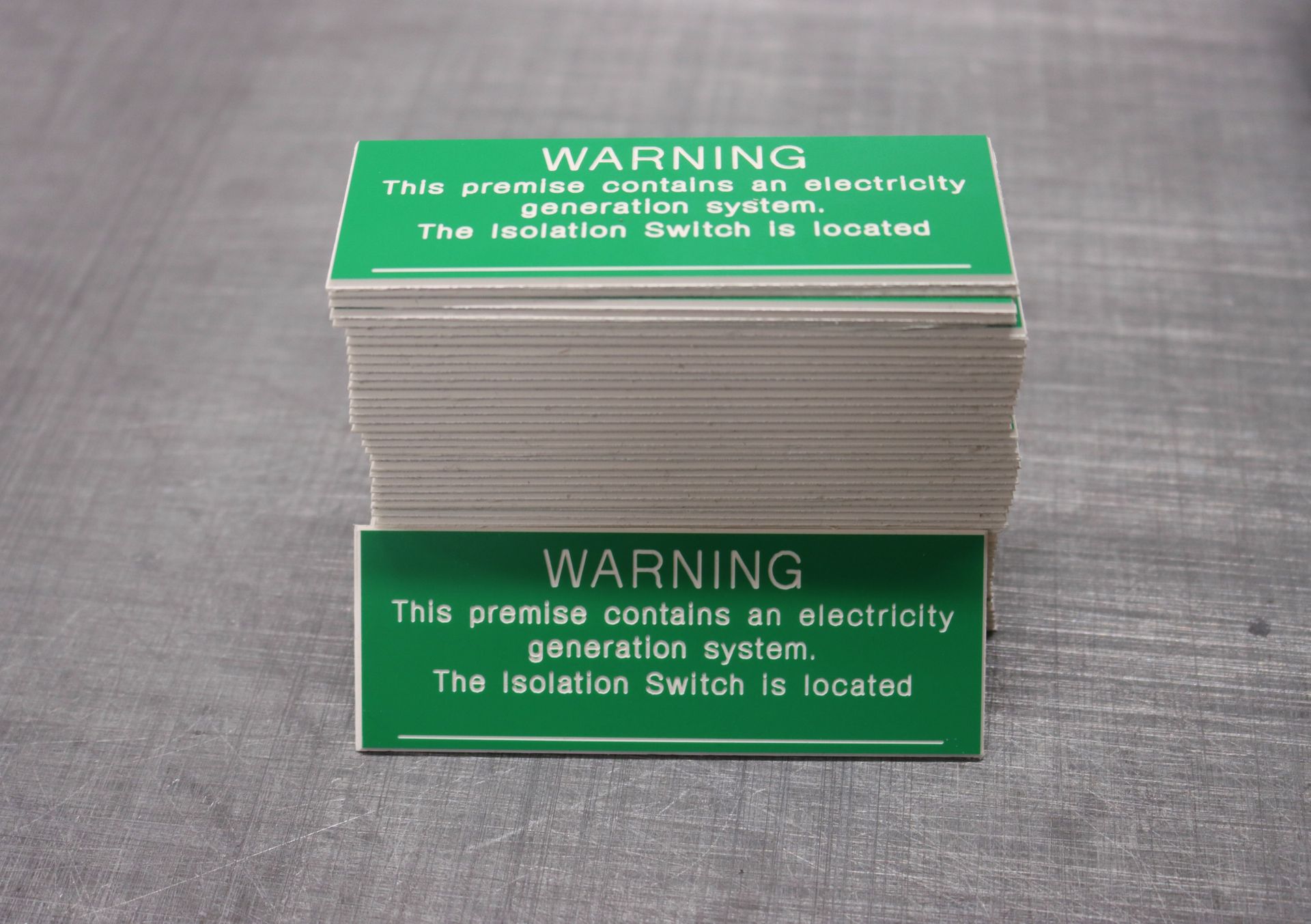A stack of green warning signs on a table — Brookes Engraving & Signs in Woonona, NSW