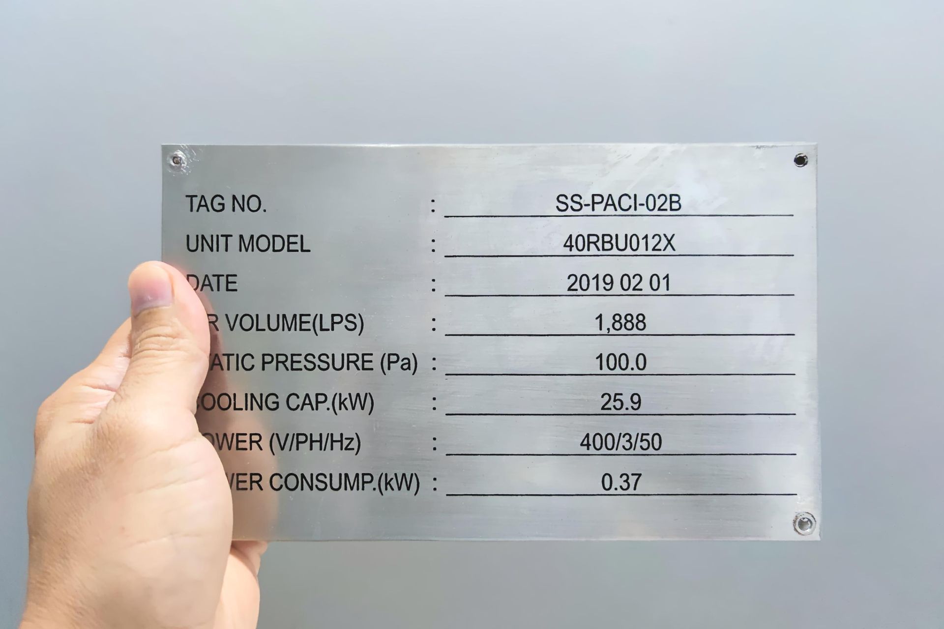 A Hand Holding a Metal Plate With Machine Specifications, Including Model, Date, and Power Consumption — Brookes Engraving & Signs in Unanderra, NSW