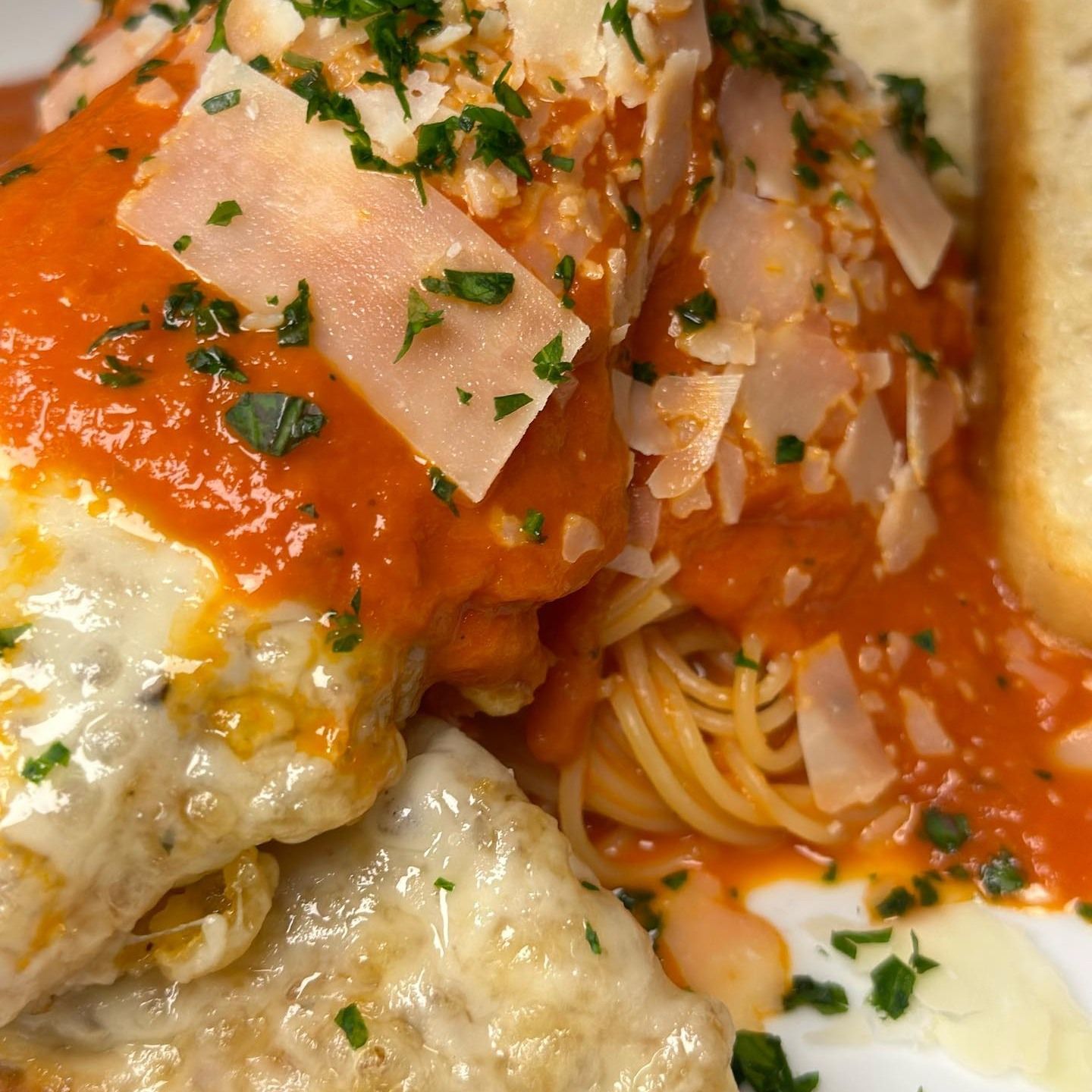 Chicken parmesan with spaghetti and tomato sauce, garnished with parsley and parmesan cheese.