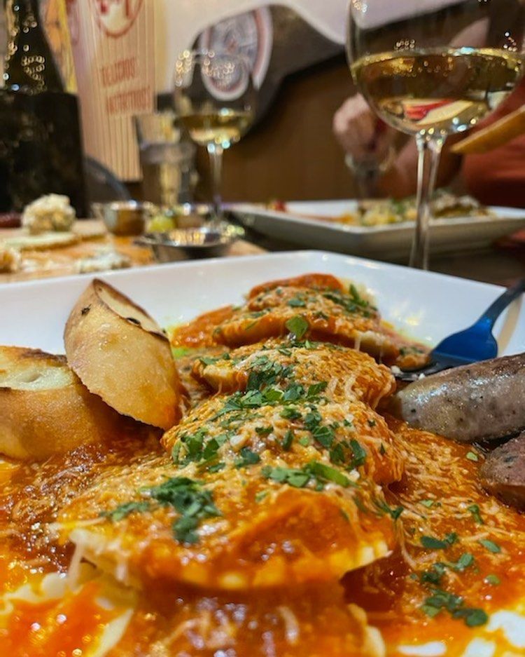 Plate of food: eggs in tomato sauce with bread and sausage, next to wine glasses.
