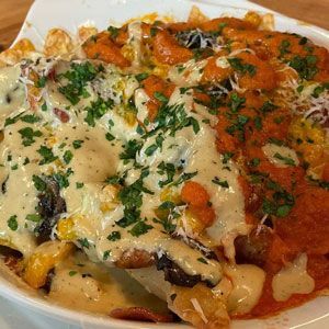 Loaded fries with creamy white sauce and orange sauce, garnished with parsley.