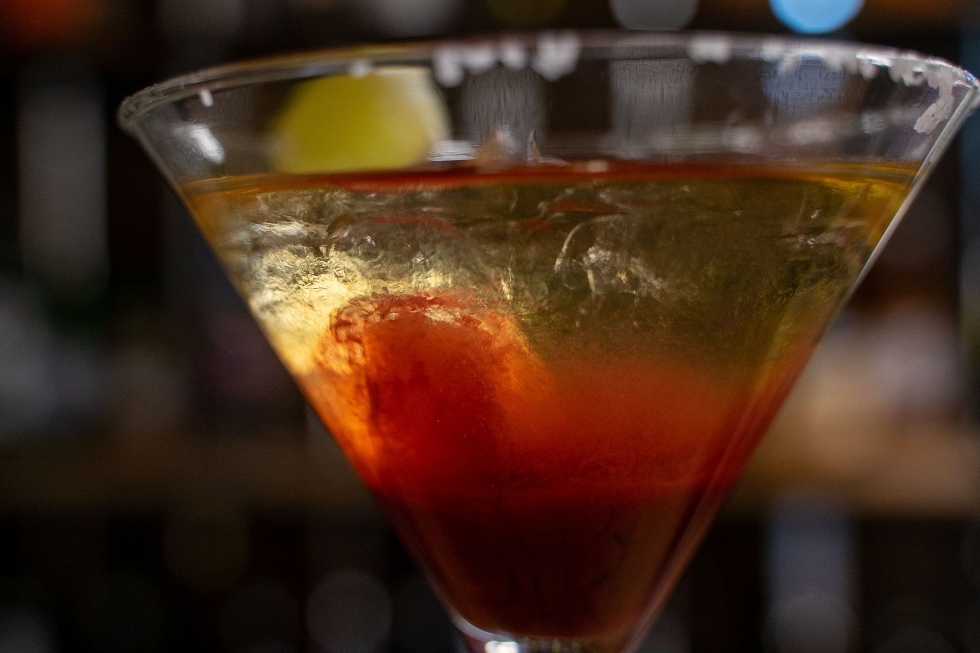 Martini glass with amber-colored drink, a large red sphere, and a green garnish.