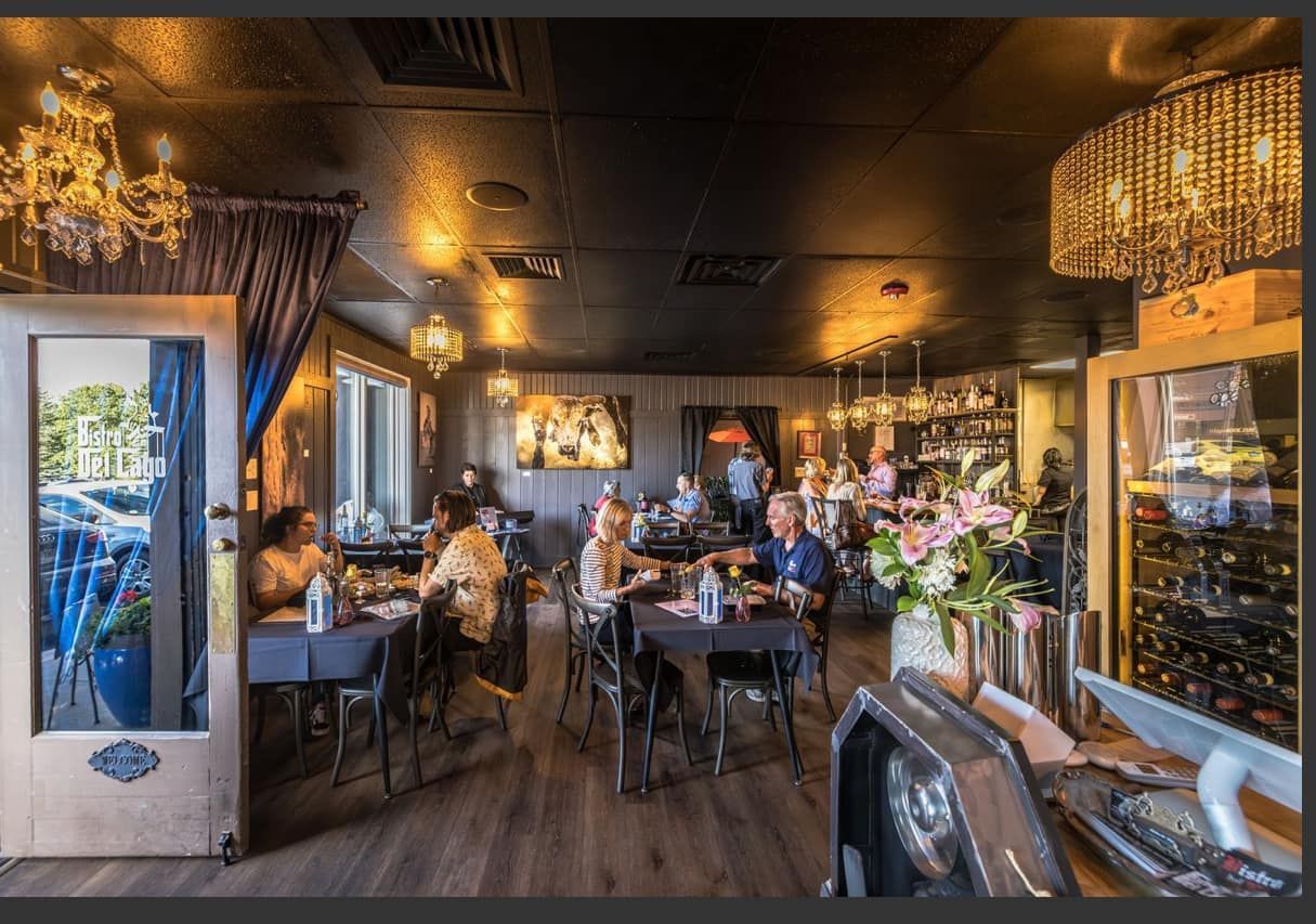 Restaurant interior with seated diners, dark walls, chandeliers, and wine display.