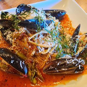 Pasta dish with mussels, red sauce, cheese, and green garnish on a white plate.