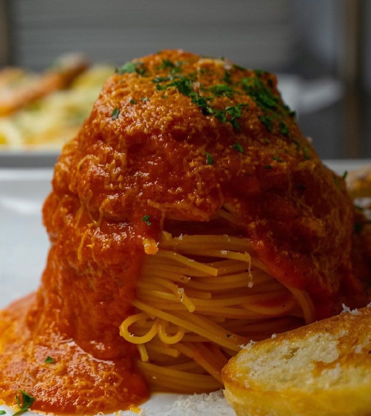 Spaghetti with red sauce piled high, garnished with parsley, served with bread.