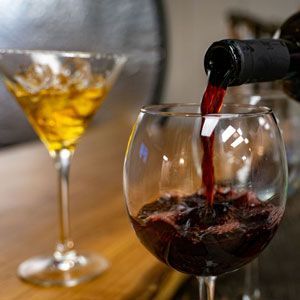 Red wine being poured into a glass, with a cocktail glass in the background.