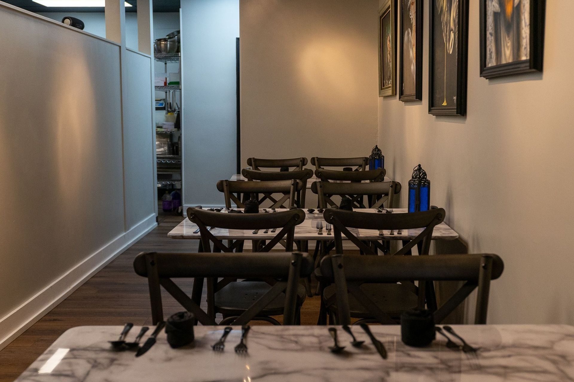 Restaurant dining room with tables set, dark chairs, and framed artwork on the wall.