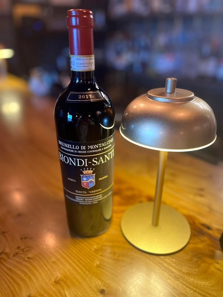 Wine bottle and gold lamp on a wooden bar. The bottle has a red top and black label.