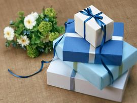 Pile of wrapped gifts in blue and white with ribbon, next to a bouquet of flowers on burlap.