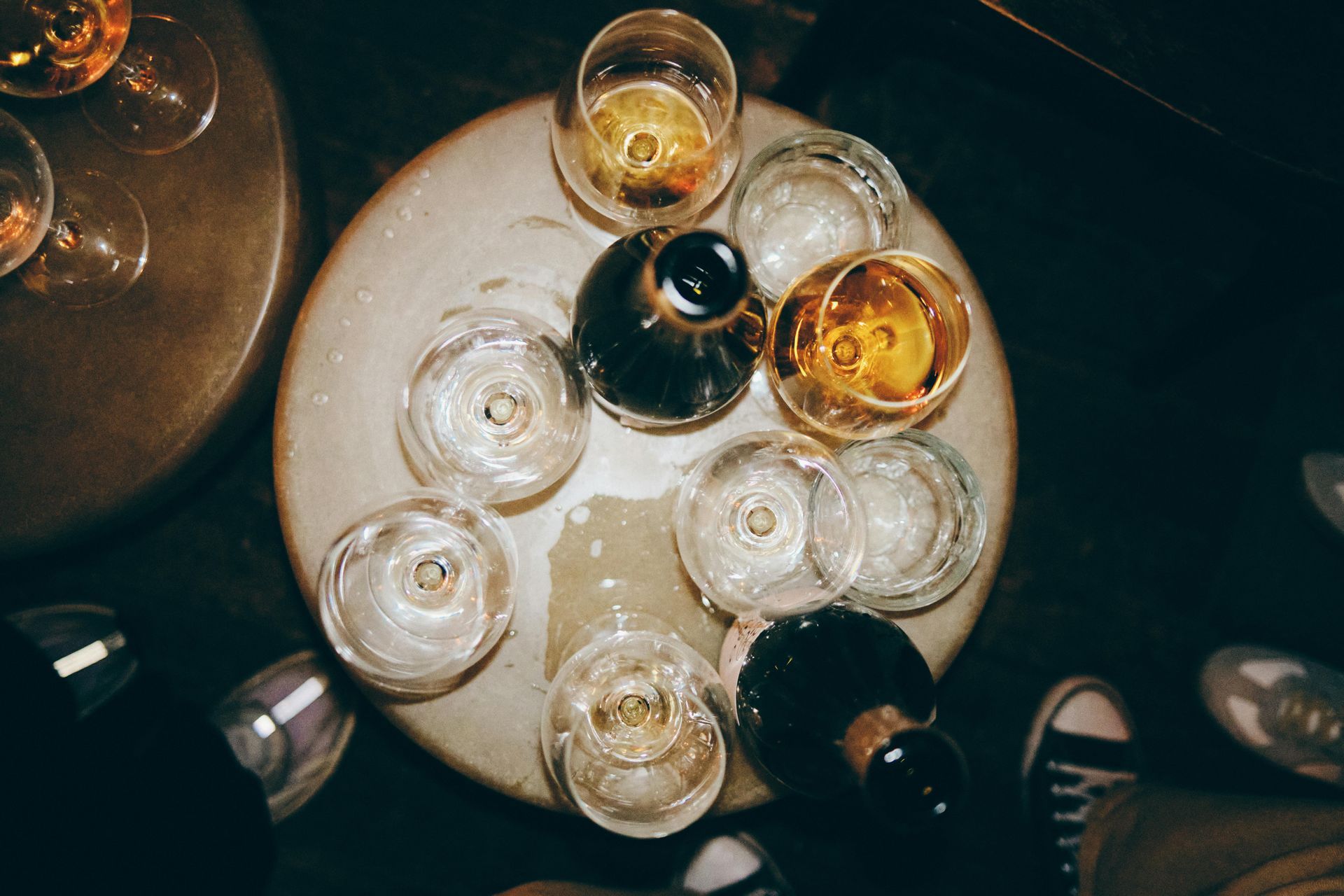 Overhead view of a round table with drinks and glasses. Champagne bottle pours into a glass.