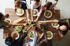 People toasting with drinks around a wooden table set with food.