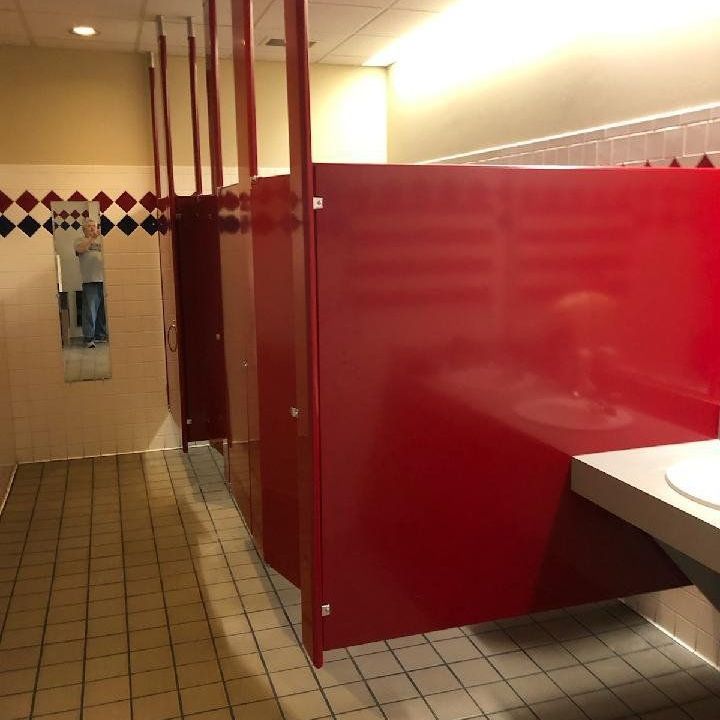 Red bathroom stalls freshly installed. They hang from the ceiling.