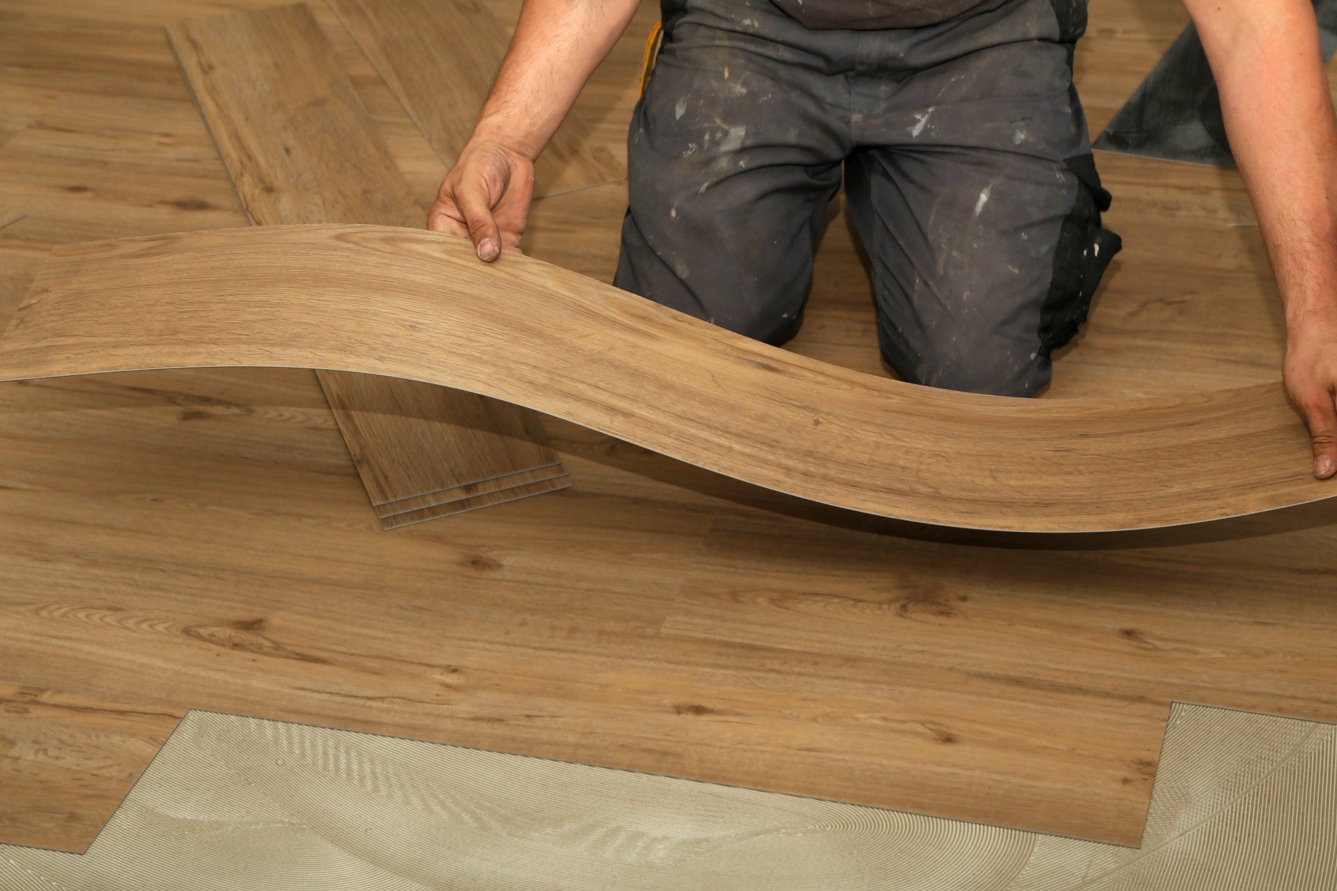 Worker carefully installing vinyl floor covering in a room, ensuring a smooth and precise fit.