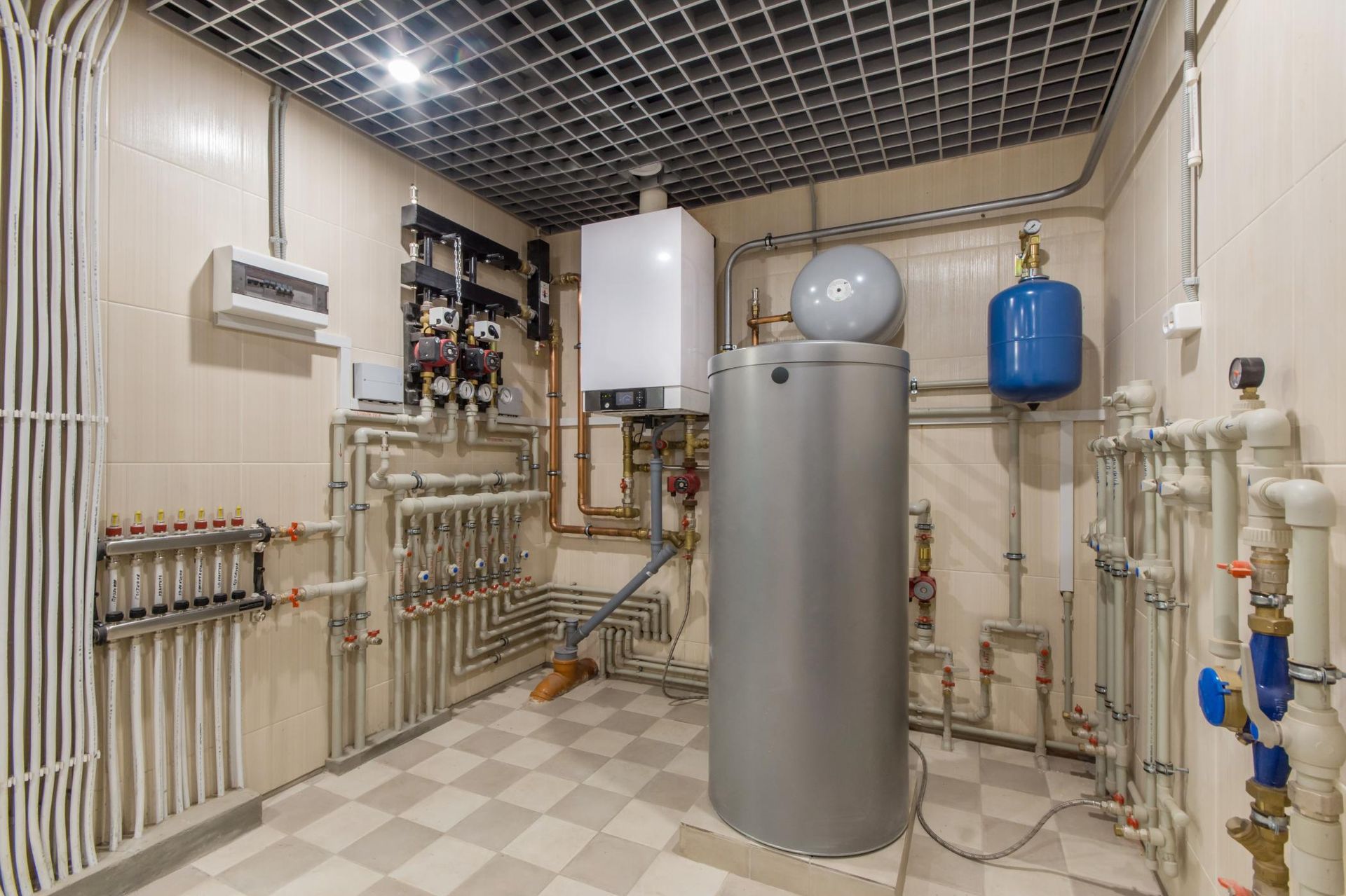 Utility room featuring a boiler, a large metal hot water tank, blue expansion tank, and intricate pipework on tiled floors.