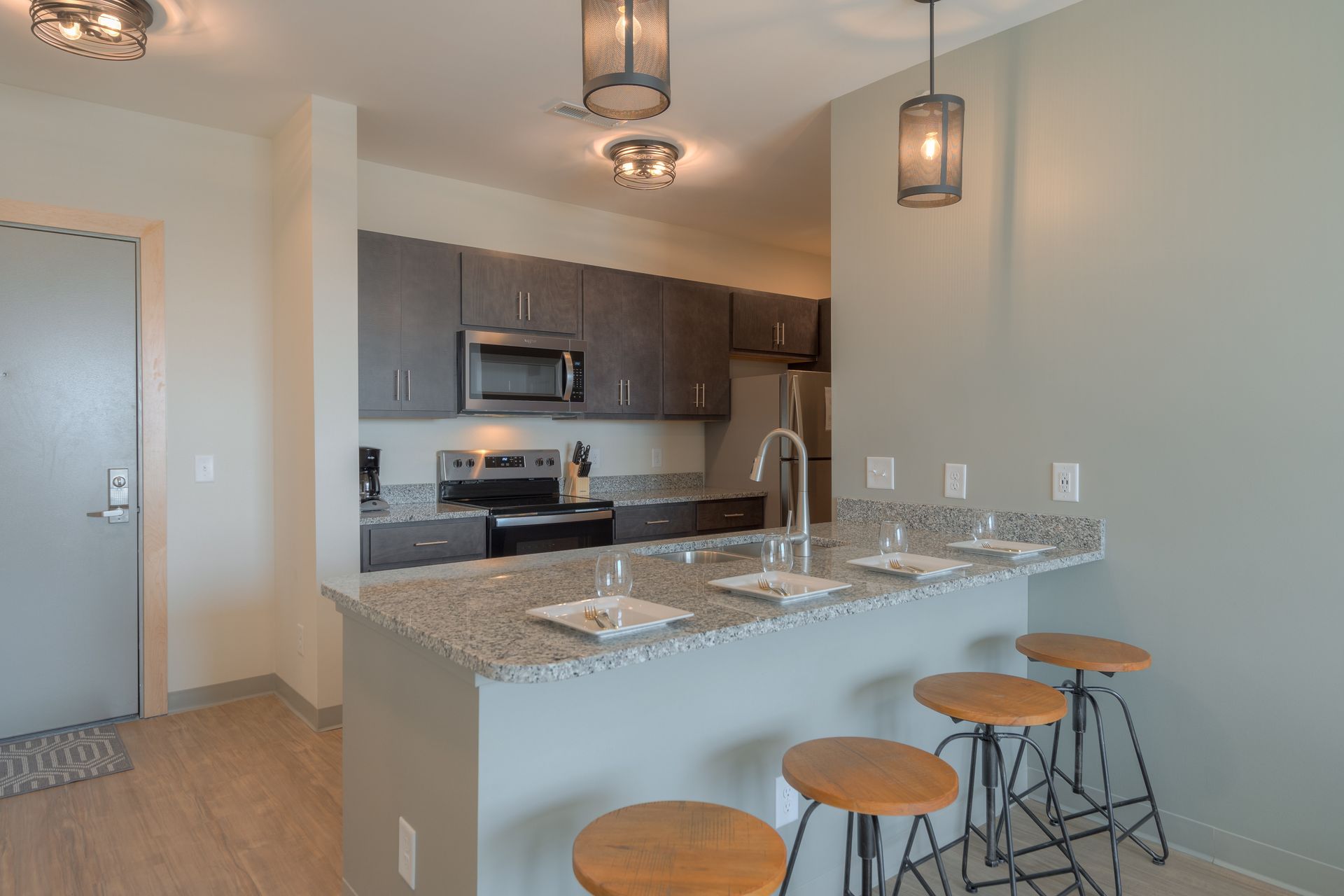 Modern kitchen with gray cabinets, granite countertop, breakfast bar, and stools.