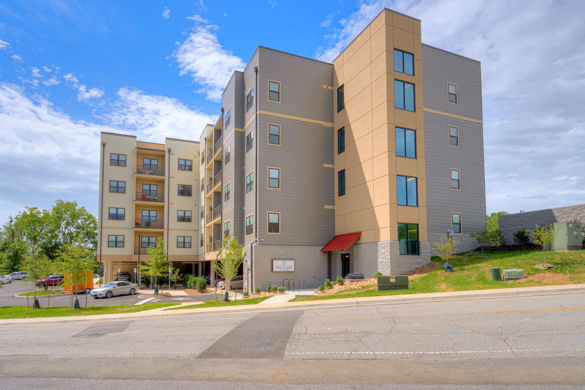 Multi-story modern apartment building with gray and tan siding under a blue sky.
