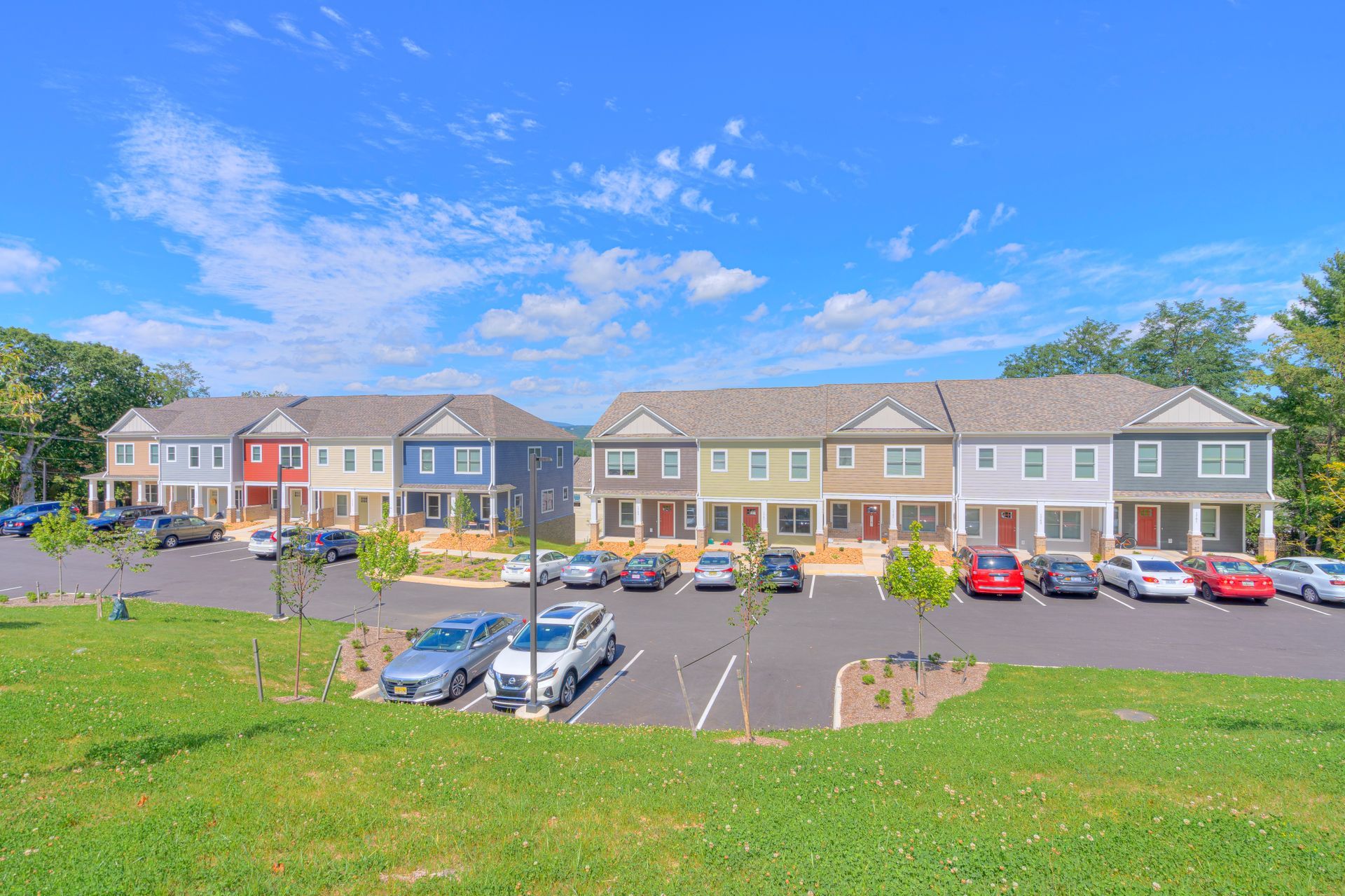 Row of colorful townhouses with parked cars on a sunny day. Green lawn in the foreground.