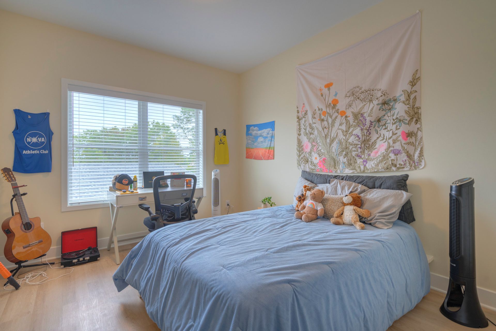 Beige living room with light wooden floors and kitchen in the background. A sofa, TV, and wall art are visible.