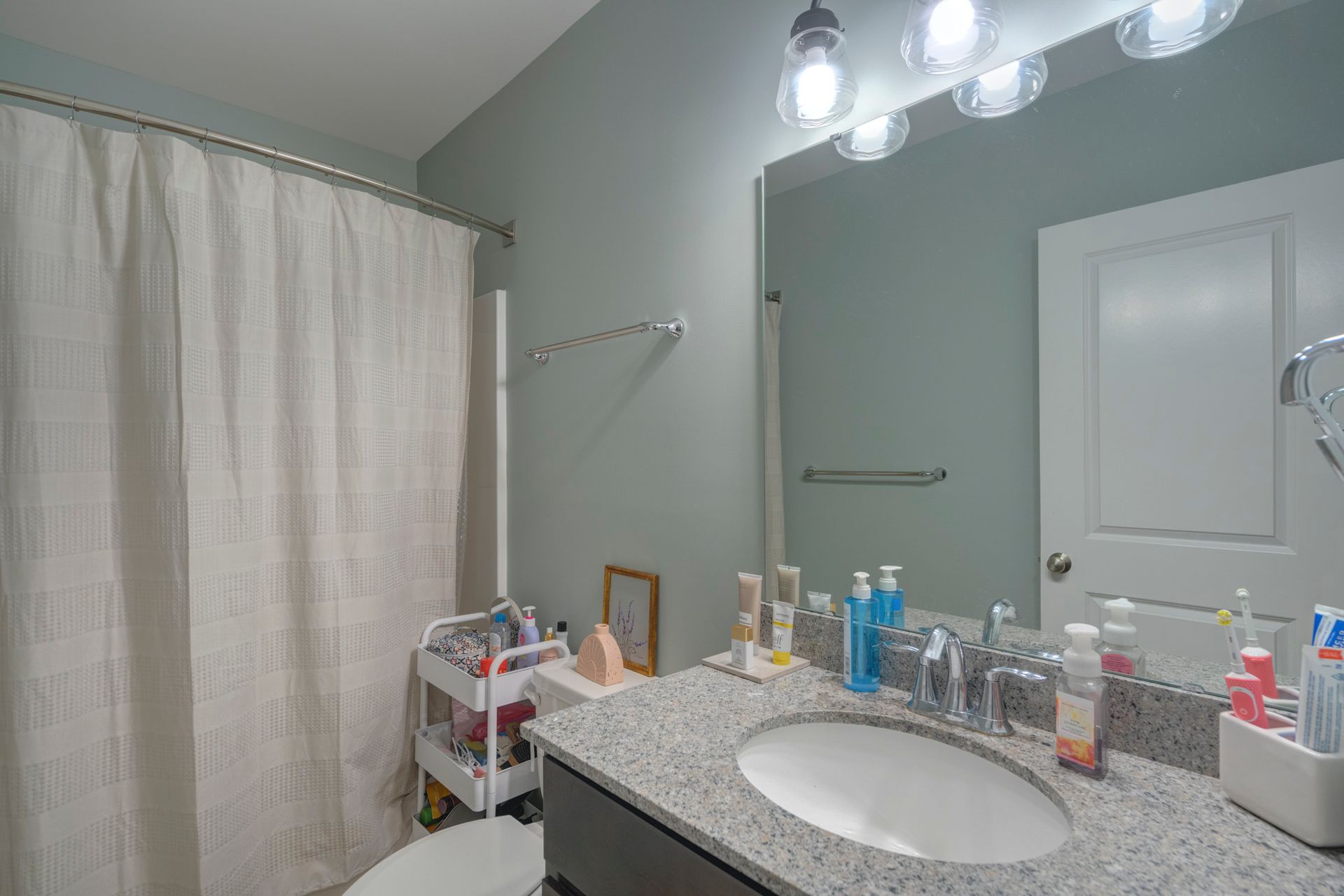 Bathroom with gray countertop, sink, mirror, shower curtain, and various toiletries.