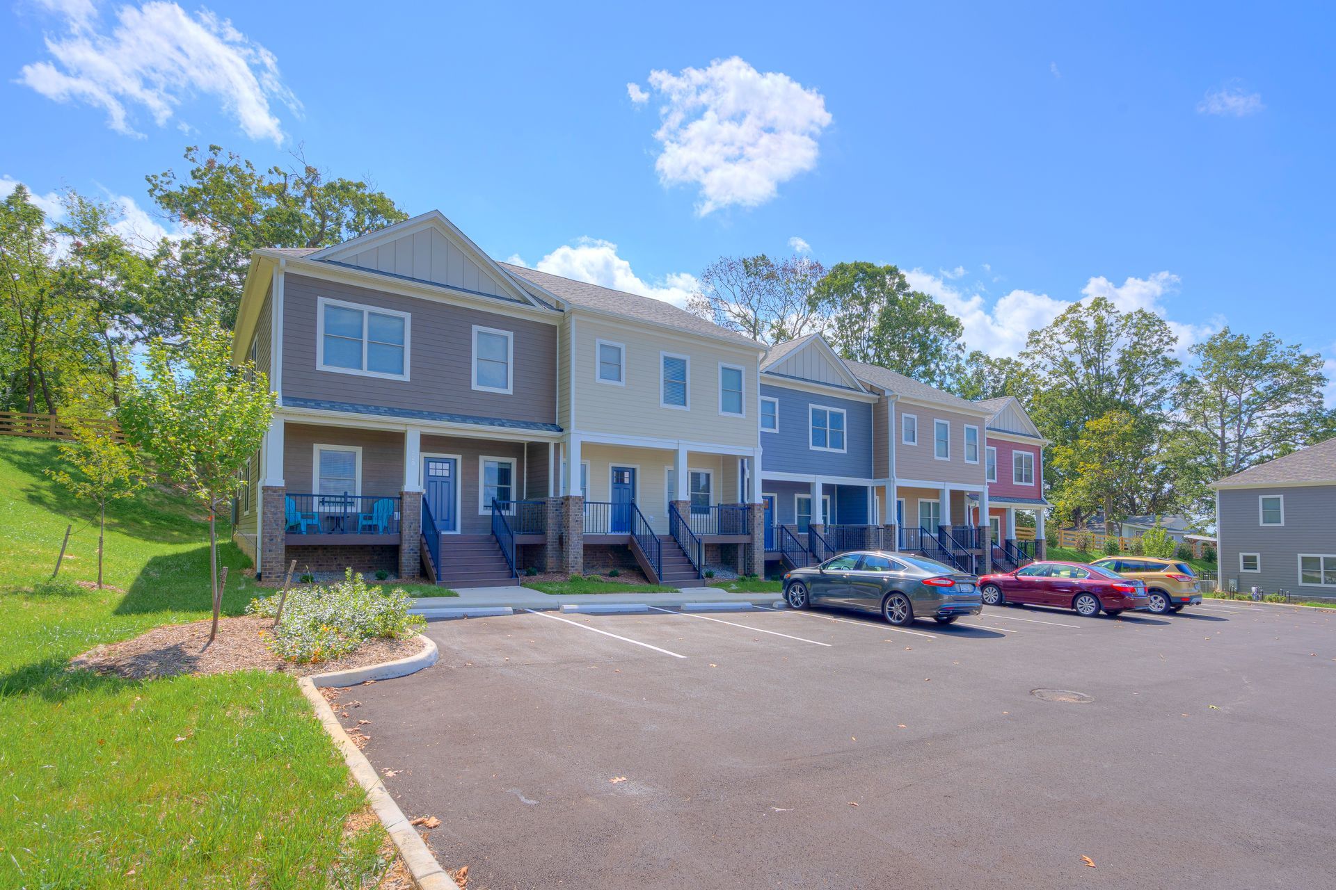 Row of colorful townhouses with parked cars in front and green lawn.