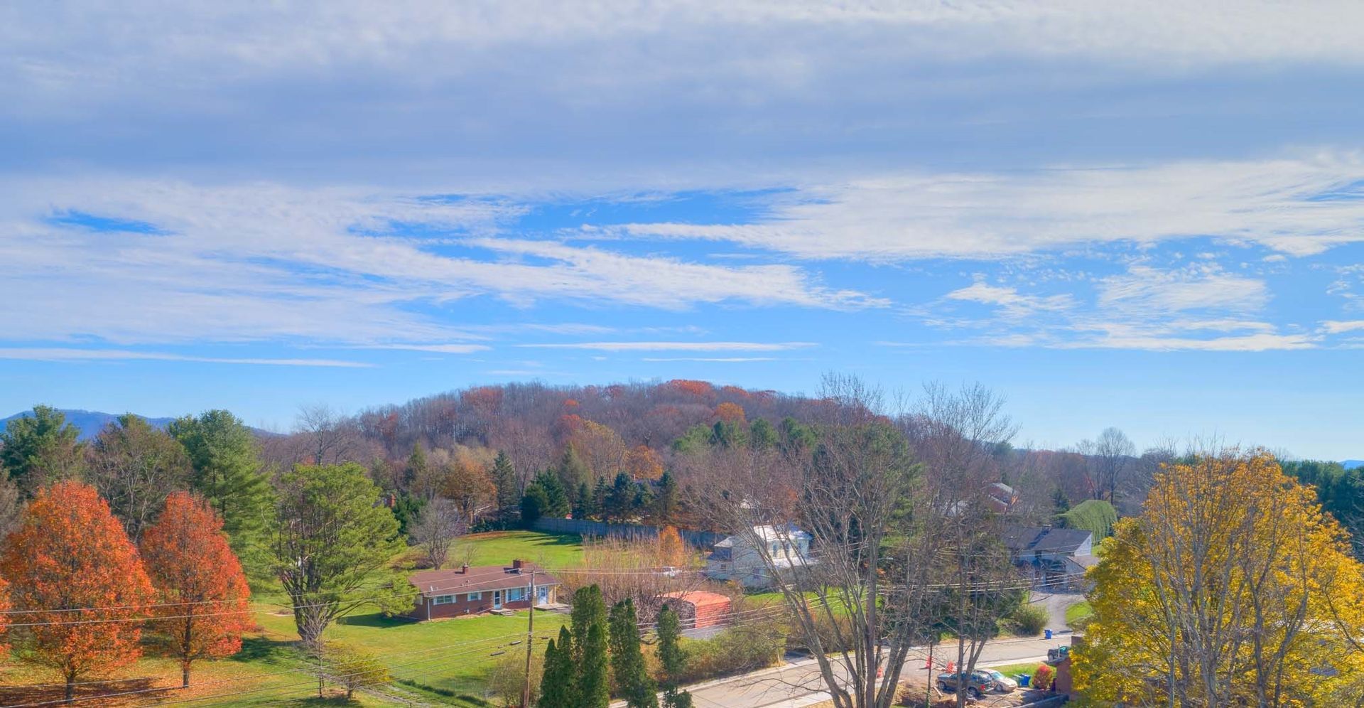Autumn landscape with colorful trees, a mountain, and a blue sky with clouds.