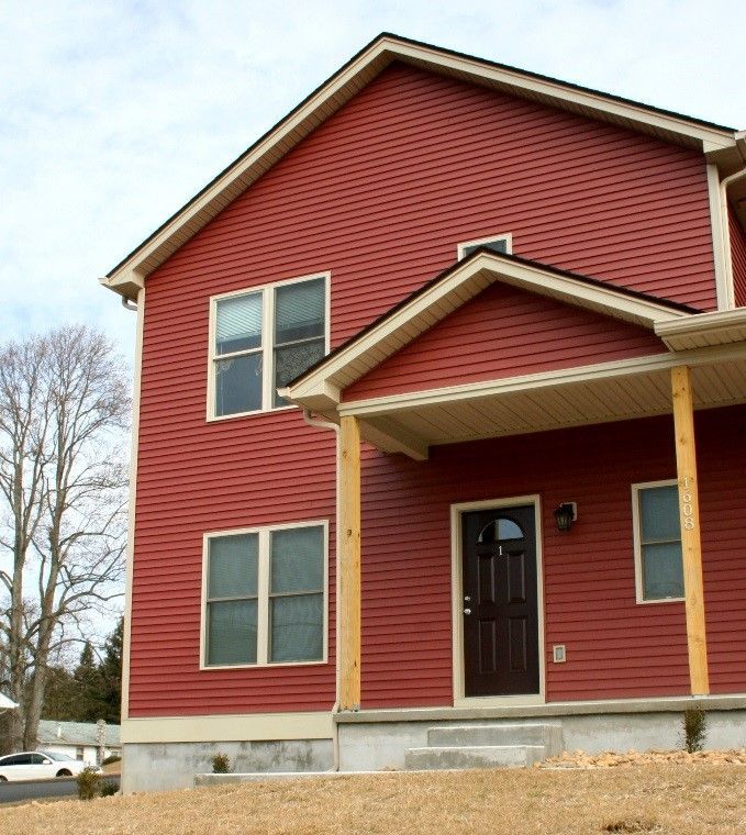 Red two-story house with a porch and brown front door, set against a cloudy sky.