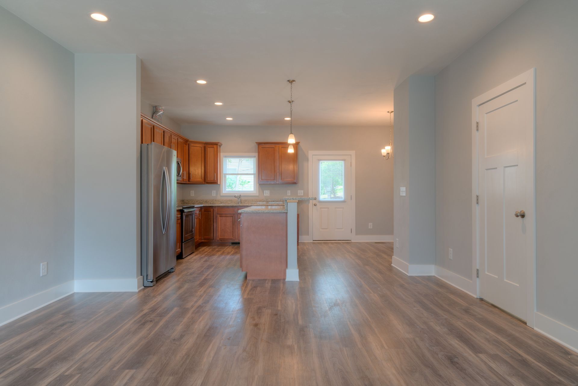Interior of a home with light blue walls, wood floors, and a kitchen with stainless steel appliances.