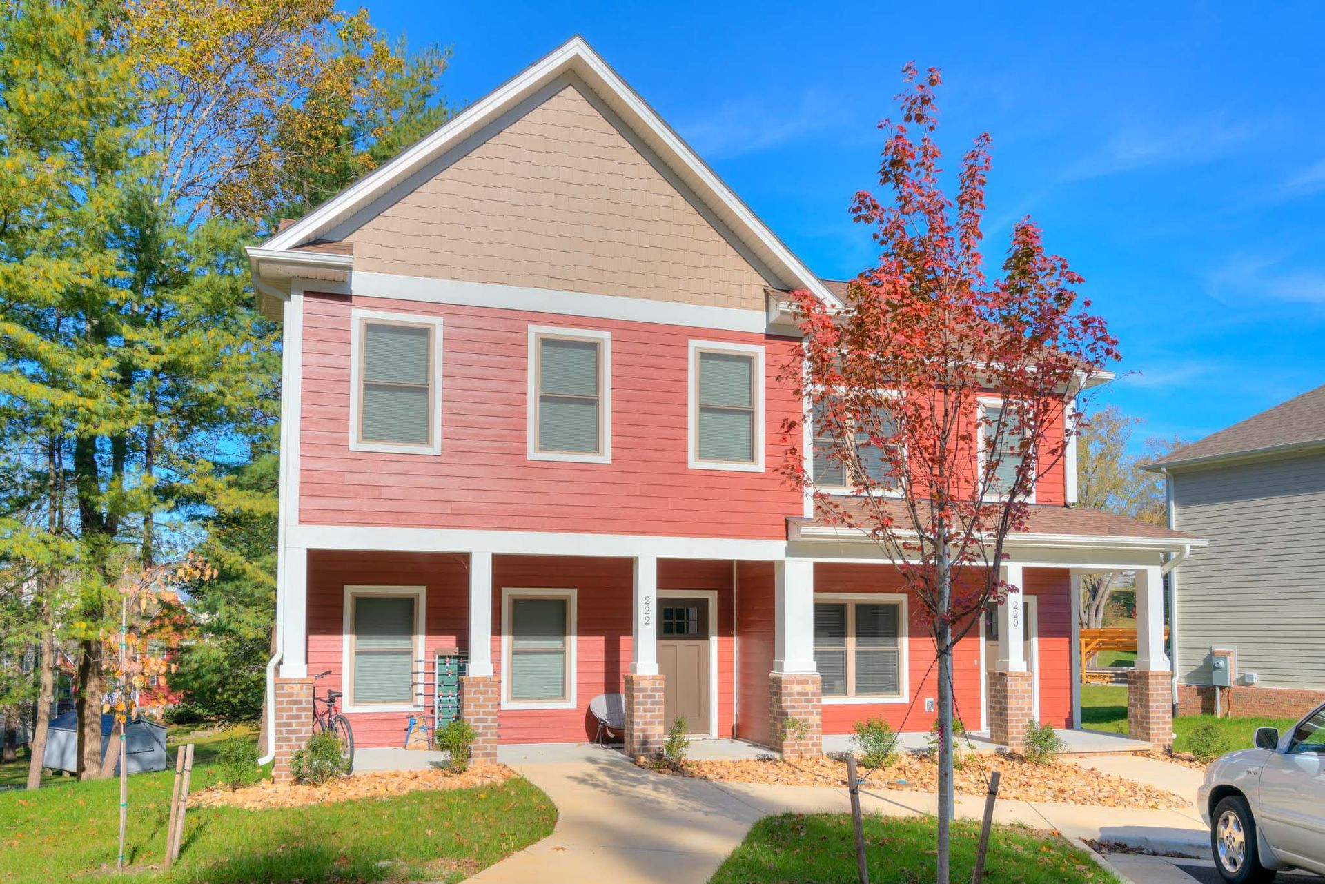 Two-story red house with beige accents and porch. Sunny day.