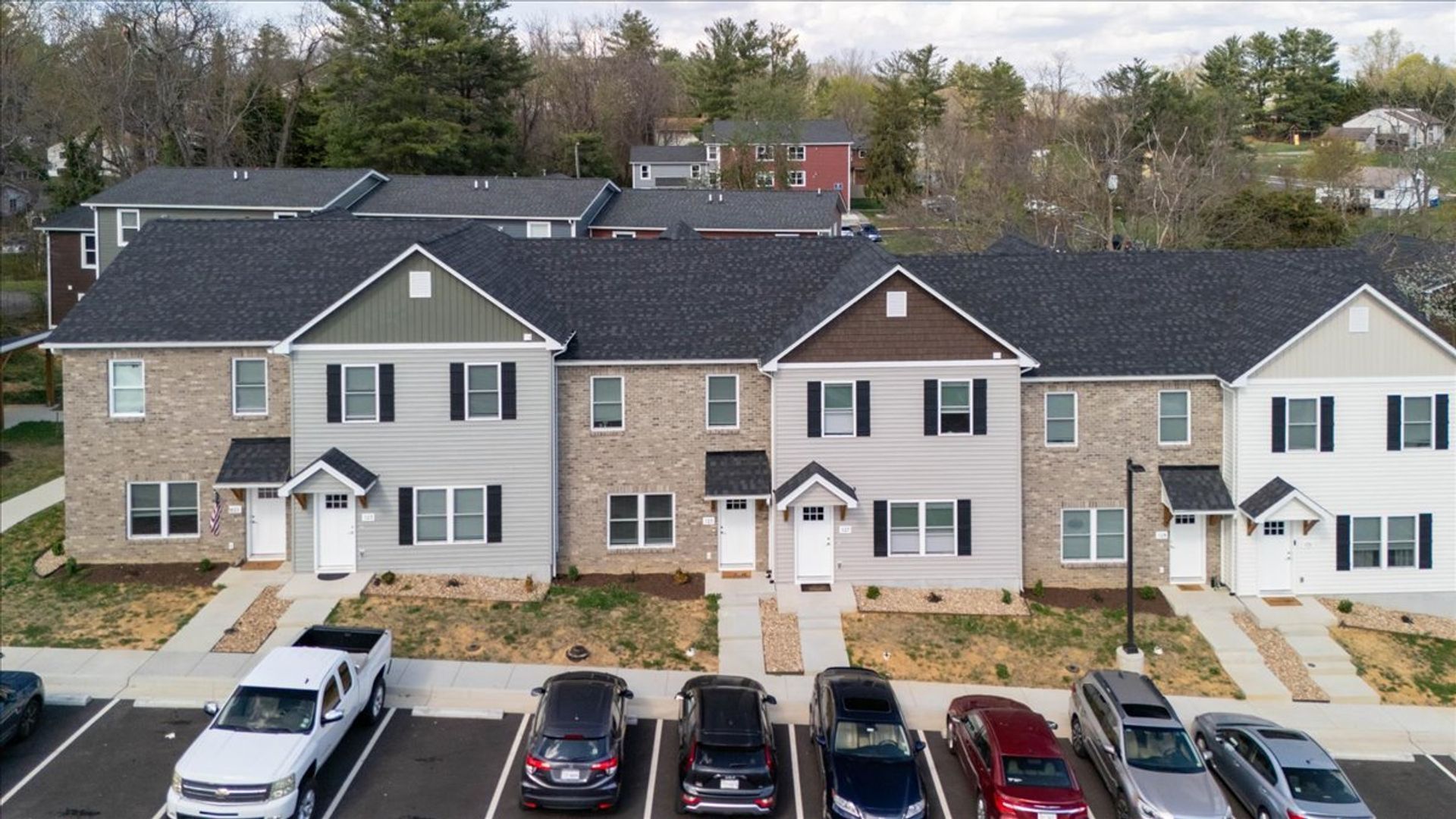 Row of townhouses with varying siding colors and parked cars in front.