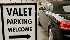 A man is opening the door of a car next to a sign that says valet parking.
