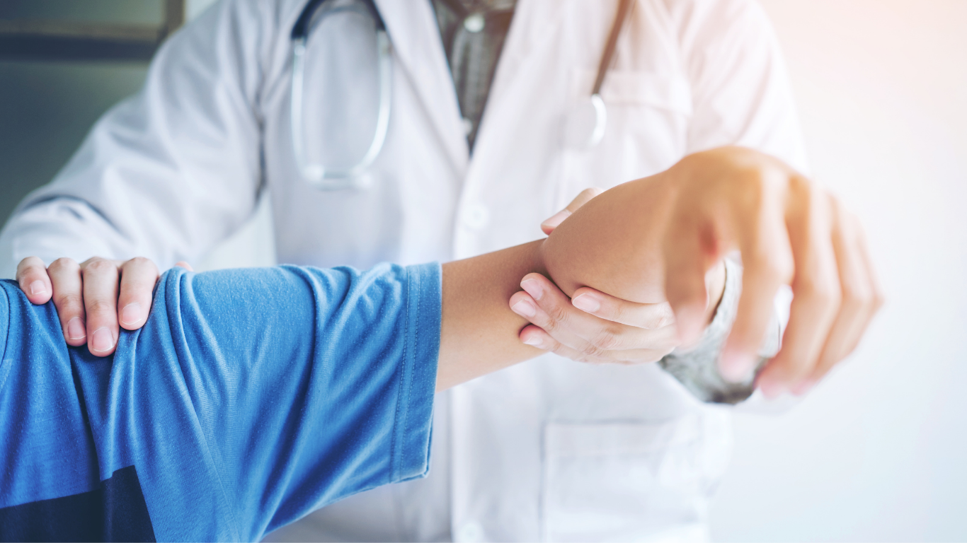Doctor examining a patient's wrist, wearing a white coat, in a bright room.