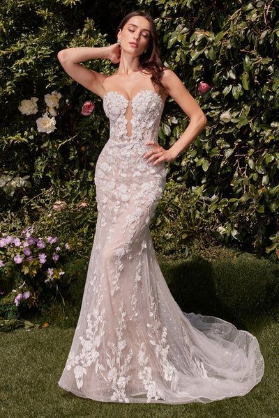 Woman in white wedding dress, eyes covered, poses outdoors with mountains in background.