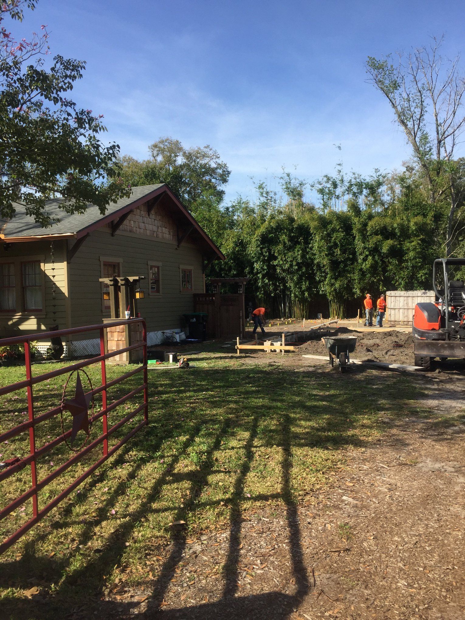 A house with a red fence in front of it is surrounded by trees and dirt.