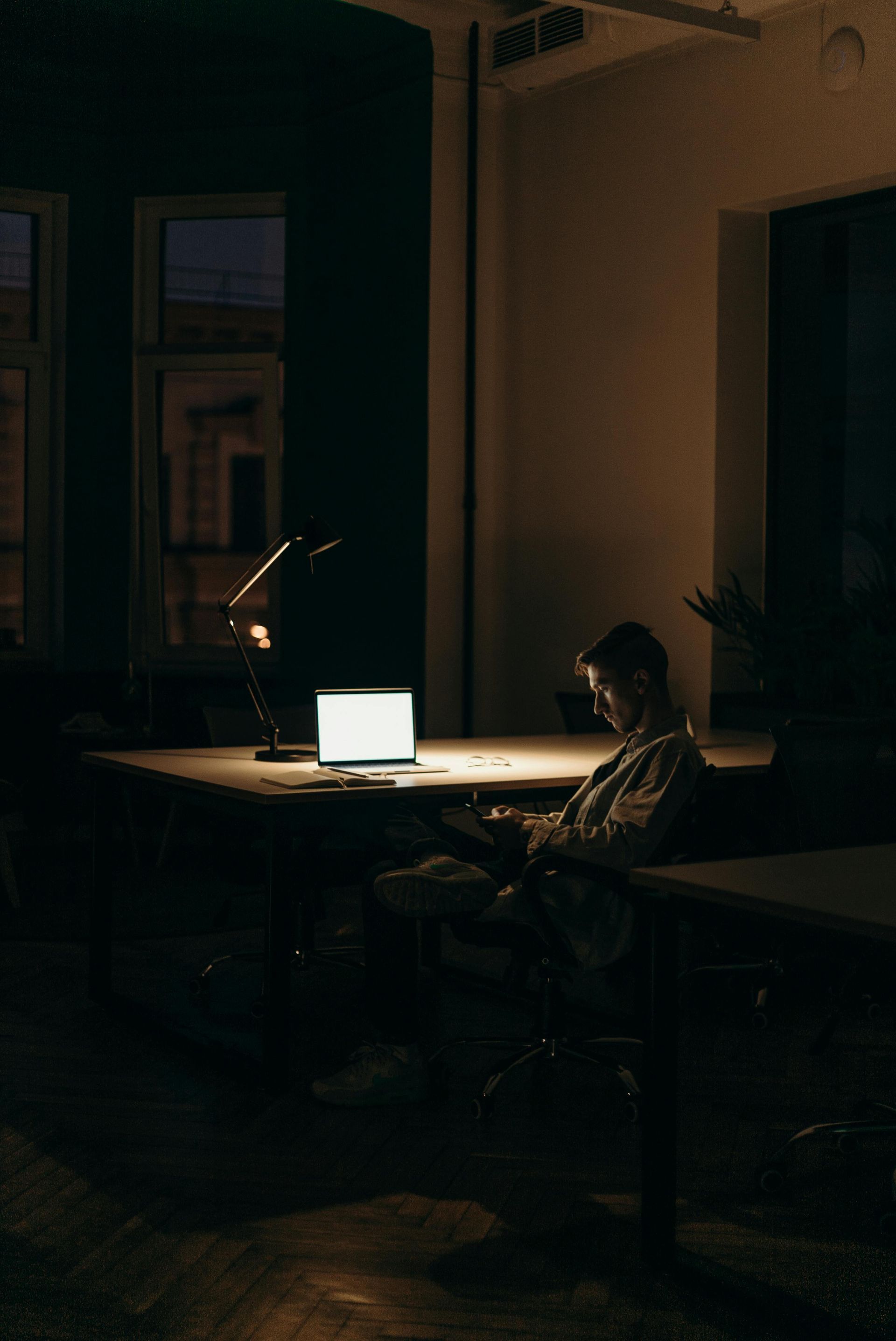 Un homme est assis à un bureau avec un ordinateur portable dans une pièce sombre.