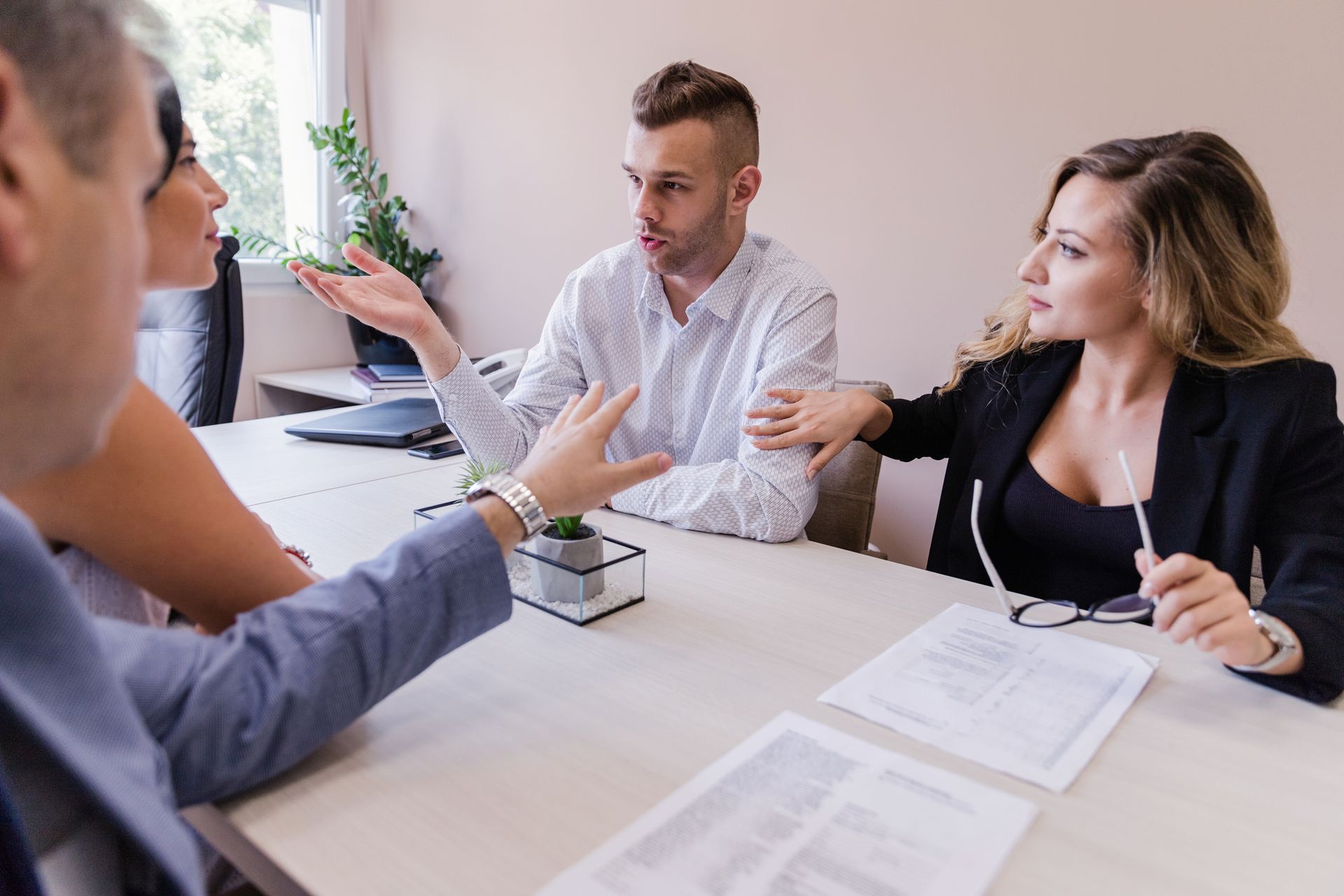 Four people in an office meeting, gesturing and discussing documents.