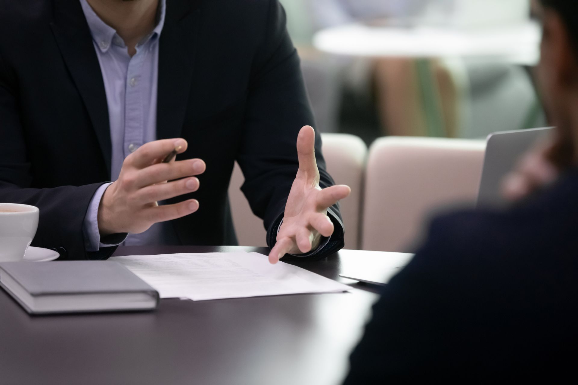 Man in a suit gestures while discussing a document with another person at a table.